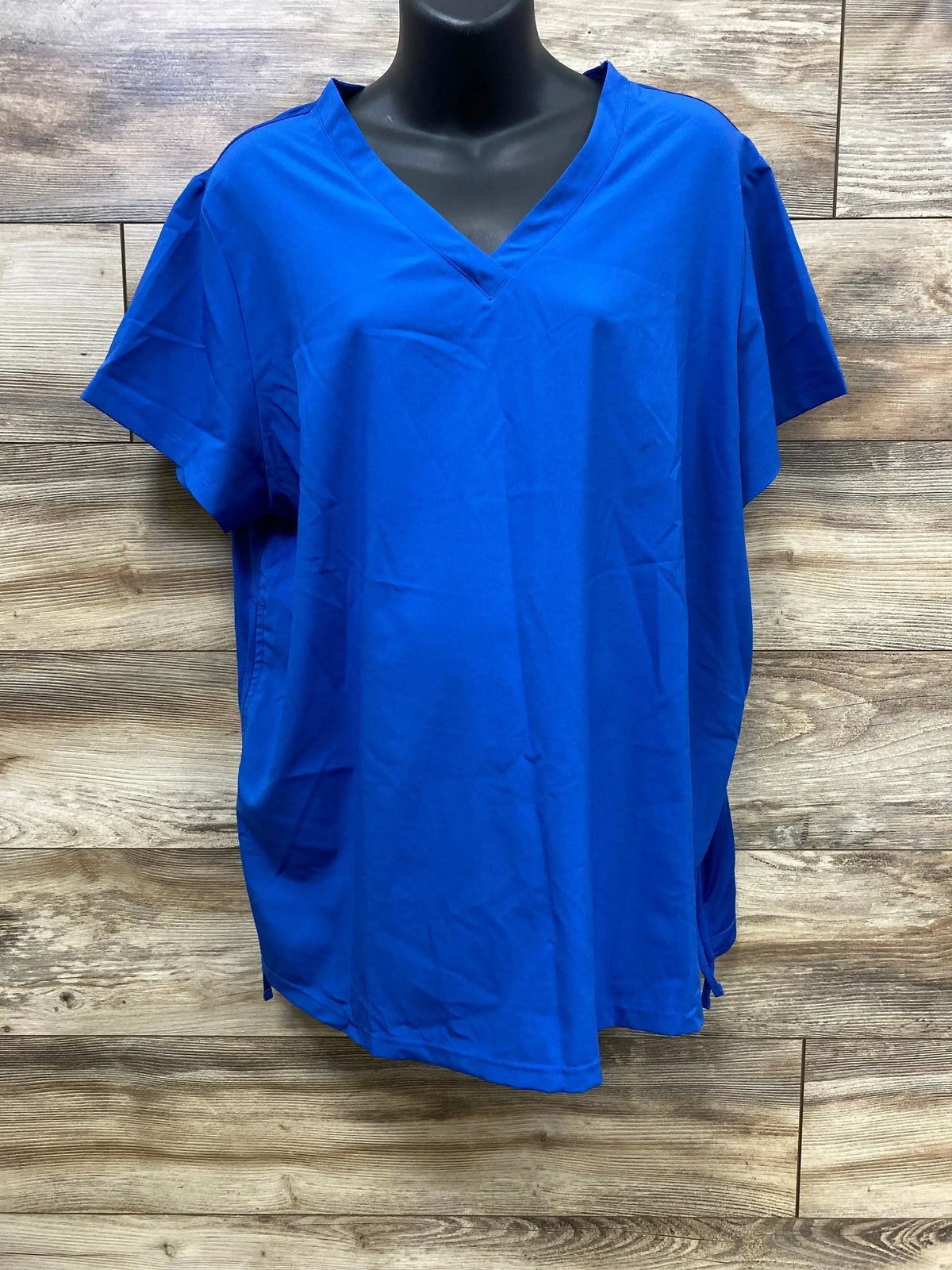 Royal blue scrub top with short sleeves and V-neck on mannequin against wood background