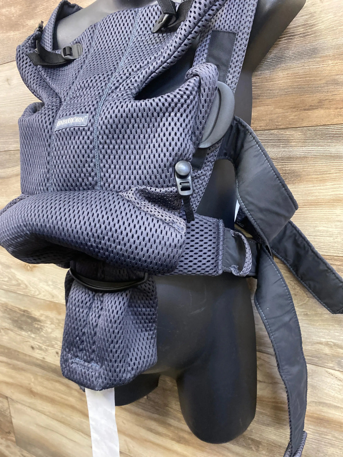 Close-up of BabyBjorn Baby Carrier Free in anthracite 3D mesh showing buckles and straps on a wood floor