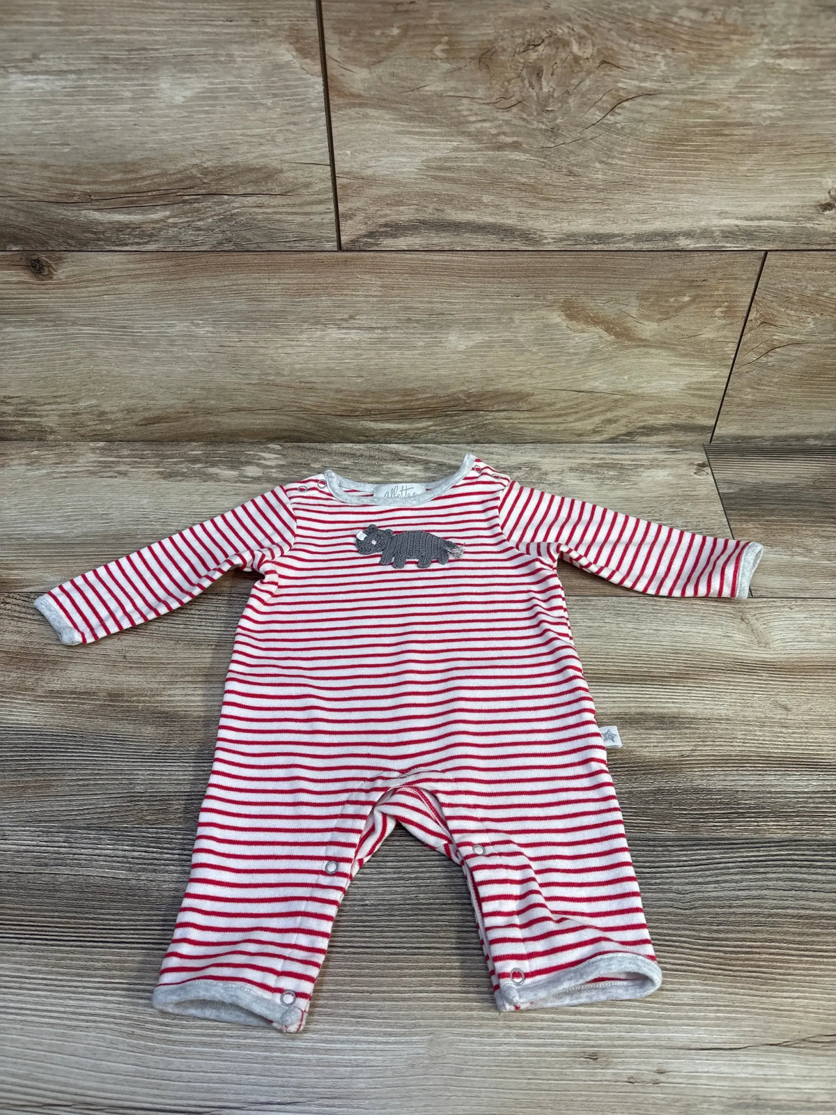 Flat lay of Albetta red and white striped long sleeve romper with crochet rhino applique on wood plank floor