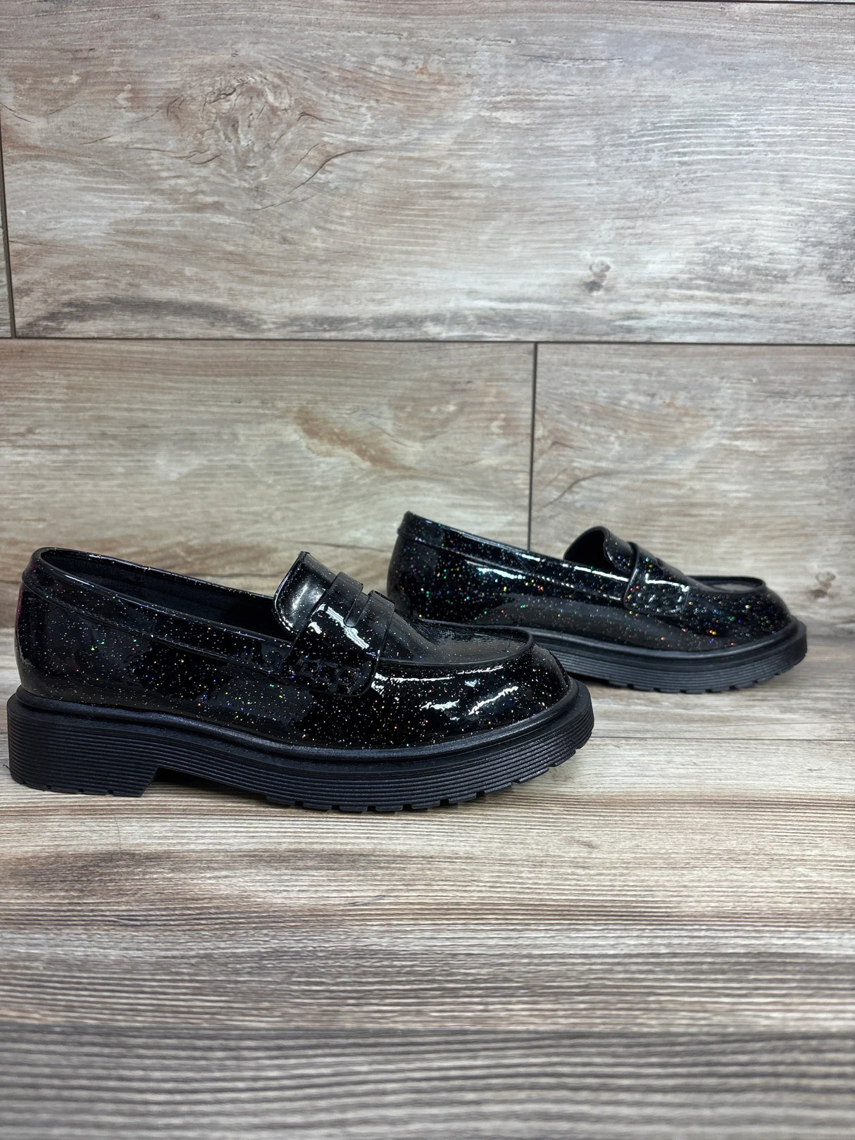 Black glitter kids loafers with chunky soles on wood floor
