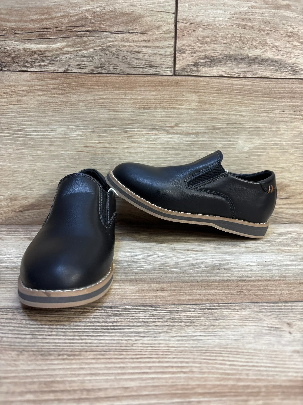 Black slip-on kids dress shoes with tan soles on wood floor