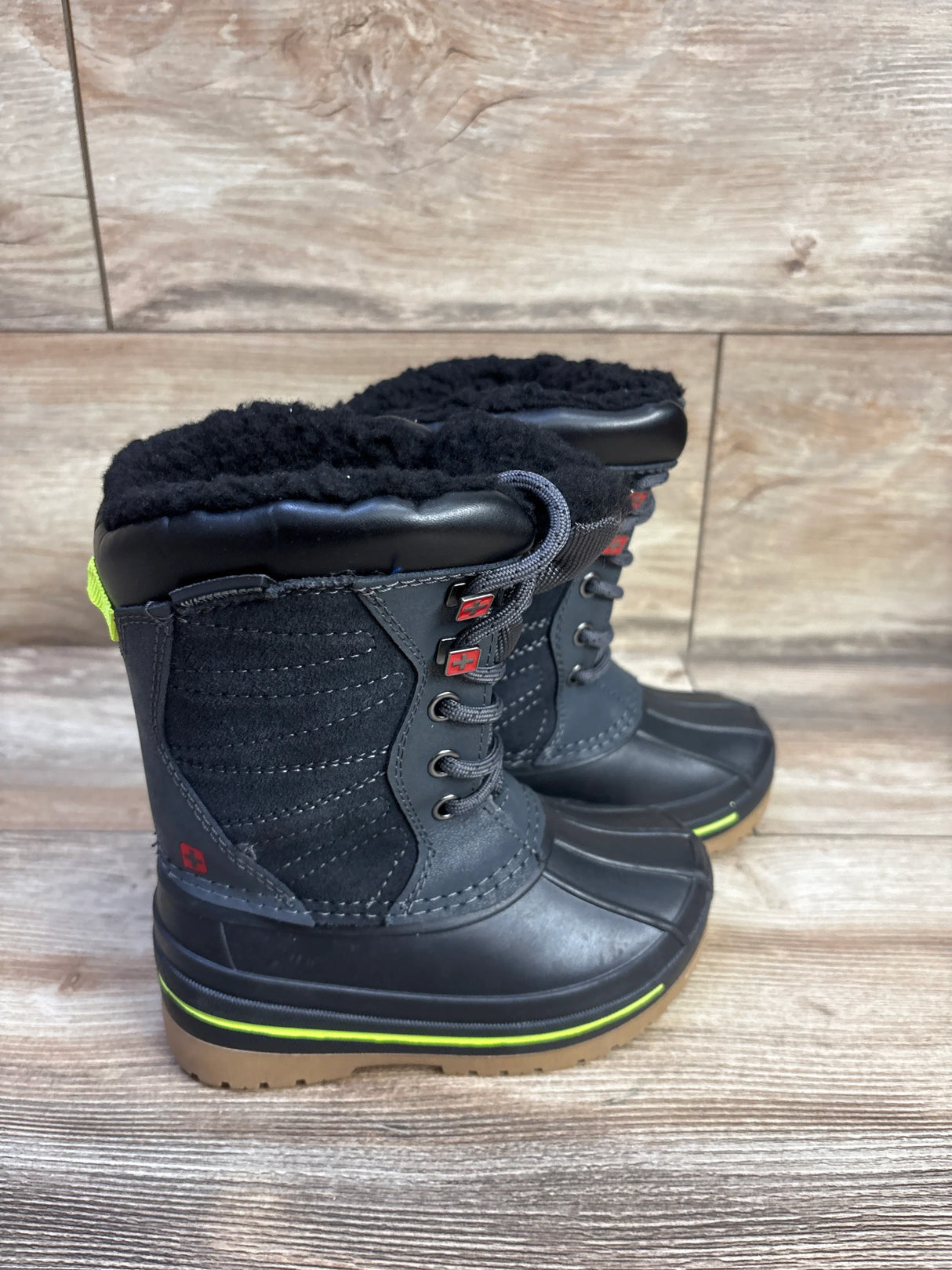 Side view of Swiss Tech black winter boots showing faux fur cuff, lace up front, rubber lower and lime green sole stripe