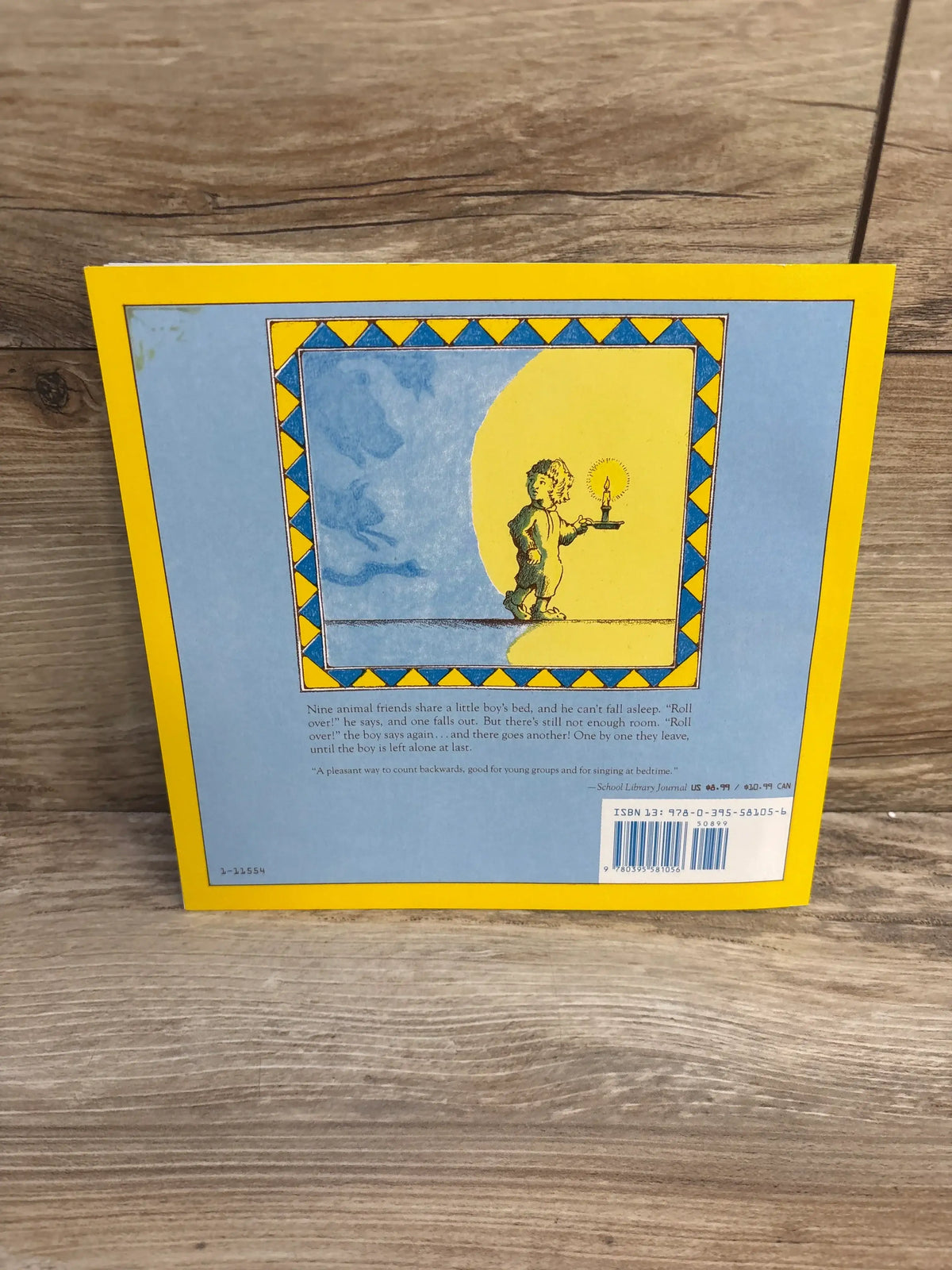 Back view of Roll Over! paperback showing blue back with yellow border, boy with candle and barcode on wood