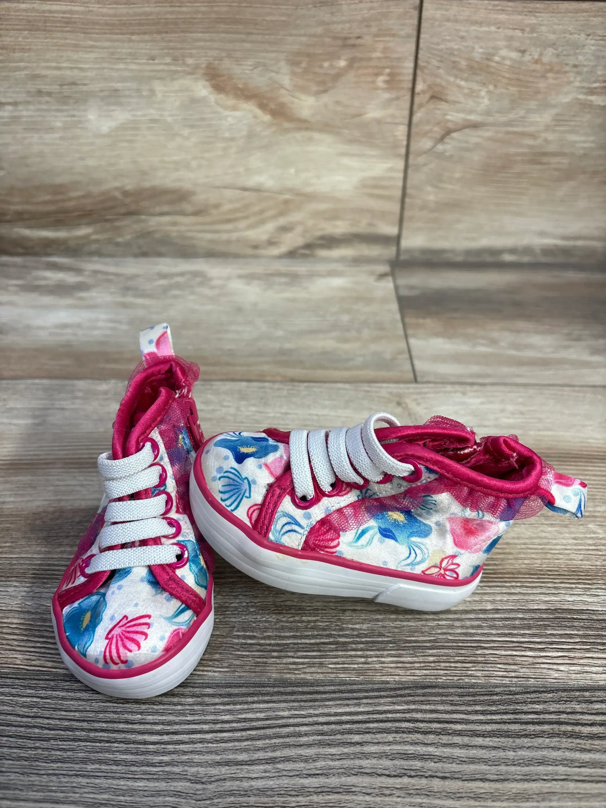 Front angled view of Disney floral high top sneakers showing pink trim, white laces and white rubber soles on wood background
