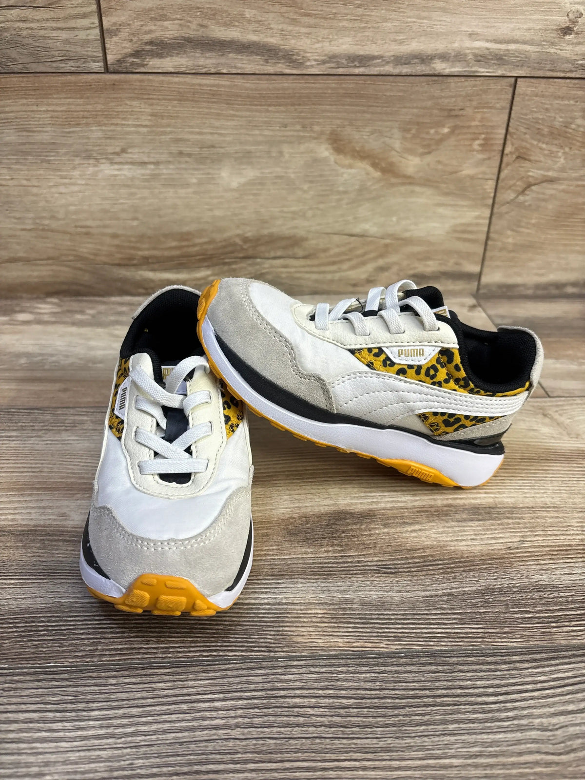 Front three-quarter view of Puma Seeker Retro Leo toddler low-top sneakers showcasing white and gray upper, yellow leopard-print accents and yellow sole on wood background