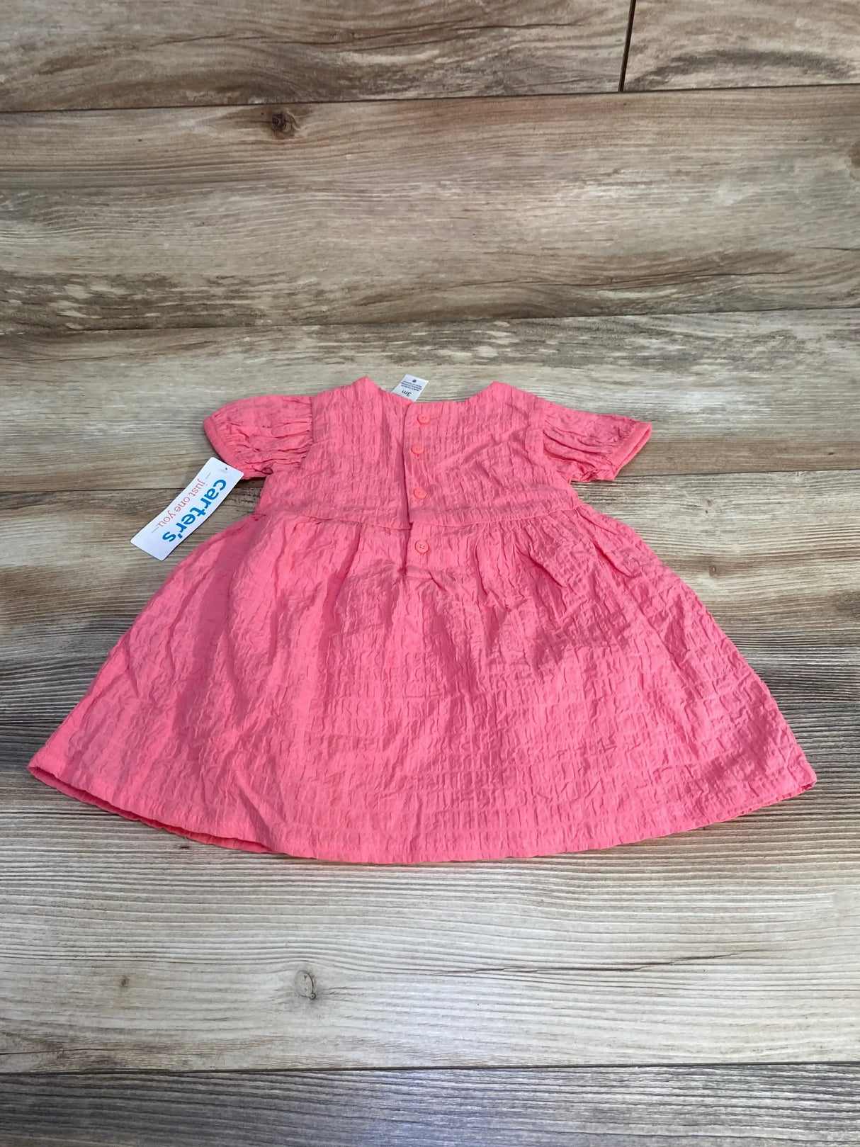 Top-down view of pink 2-piece baby dress and bloomers showing crinkled texture, puff sleeves, and back button closure on wooden background