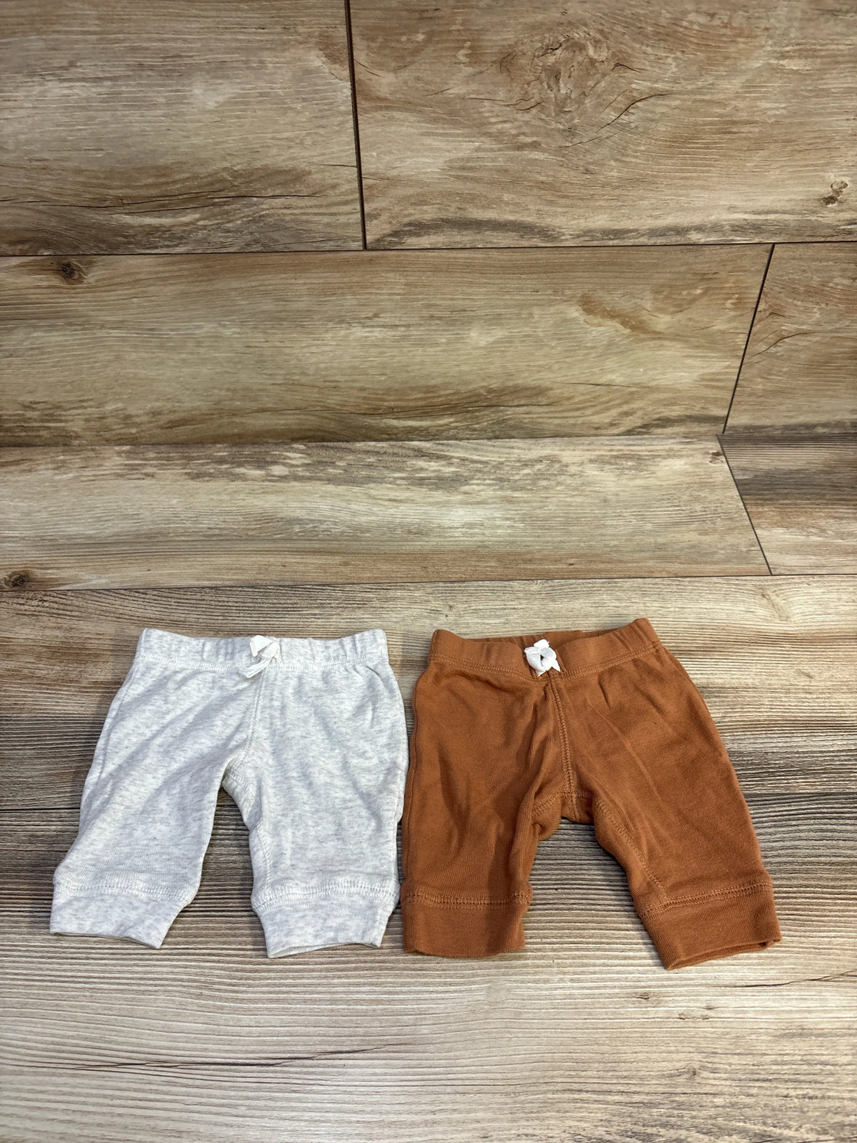Top-down view of two newborn pants showing elastic waists with small white bows on wooden floor background