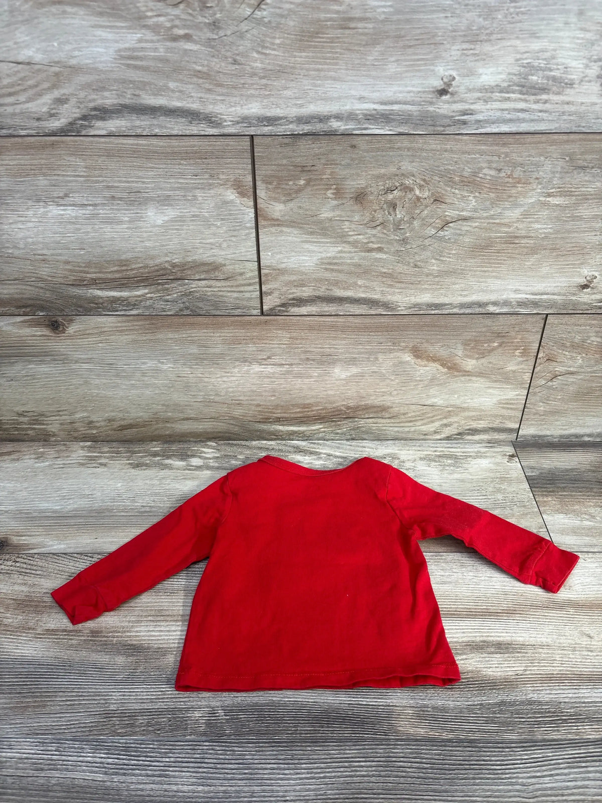 Flat lay back view of red Nike long-sleeve baby shirt with crew neck and cuffed sleeves on wood background, size 9 months