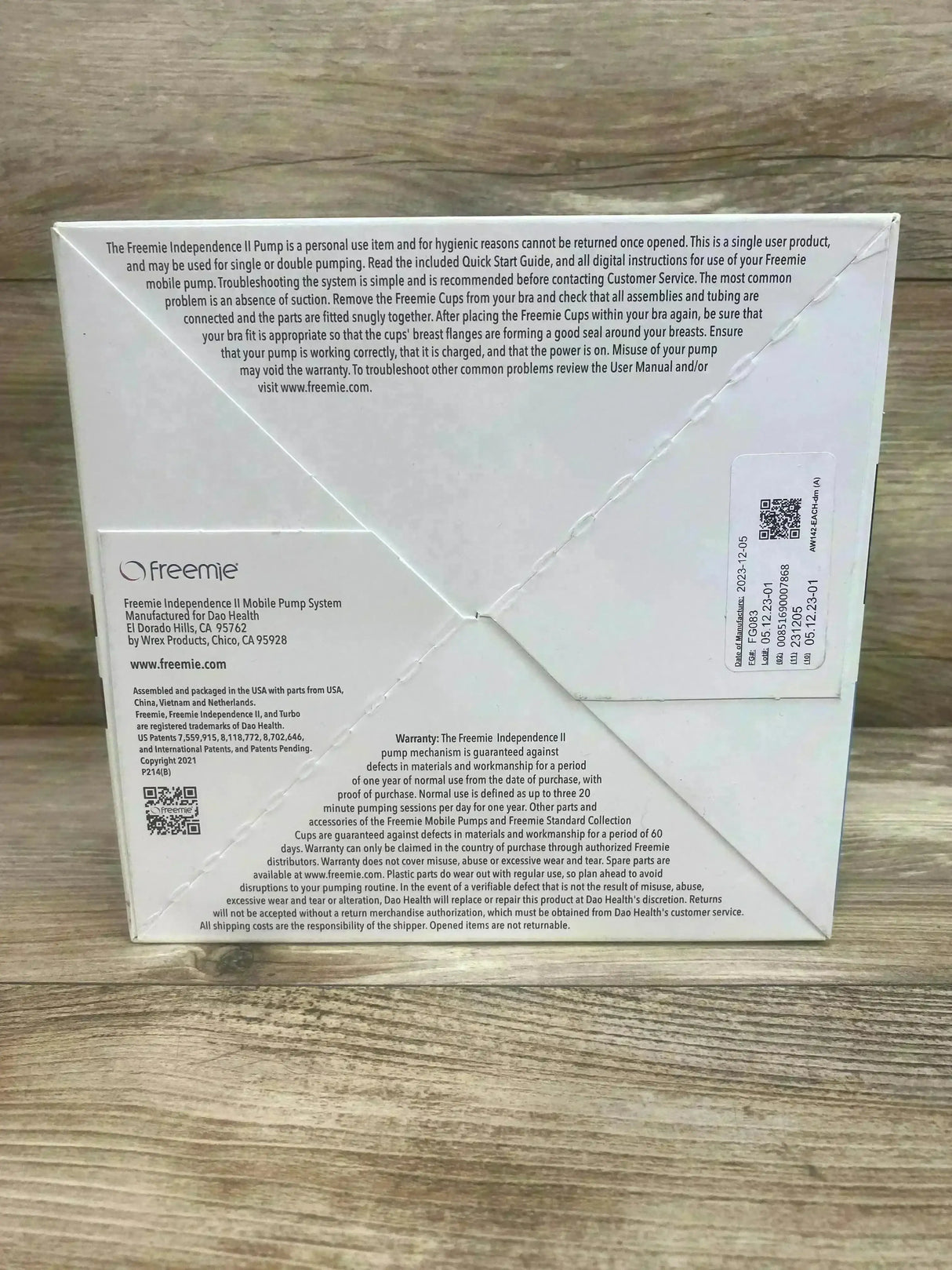 Rear view of Freemie Independence II Standard breast pump box showcasing warranty and manufacturer text with QR codes on a wood tabletop background