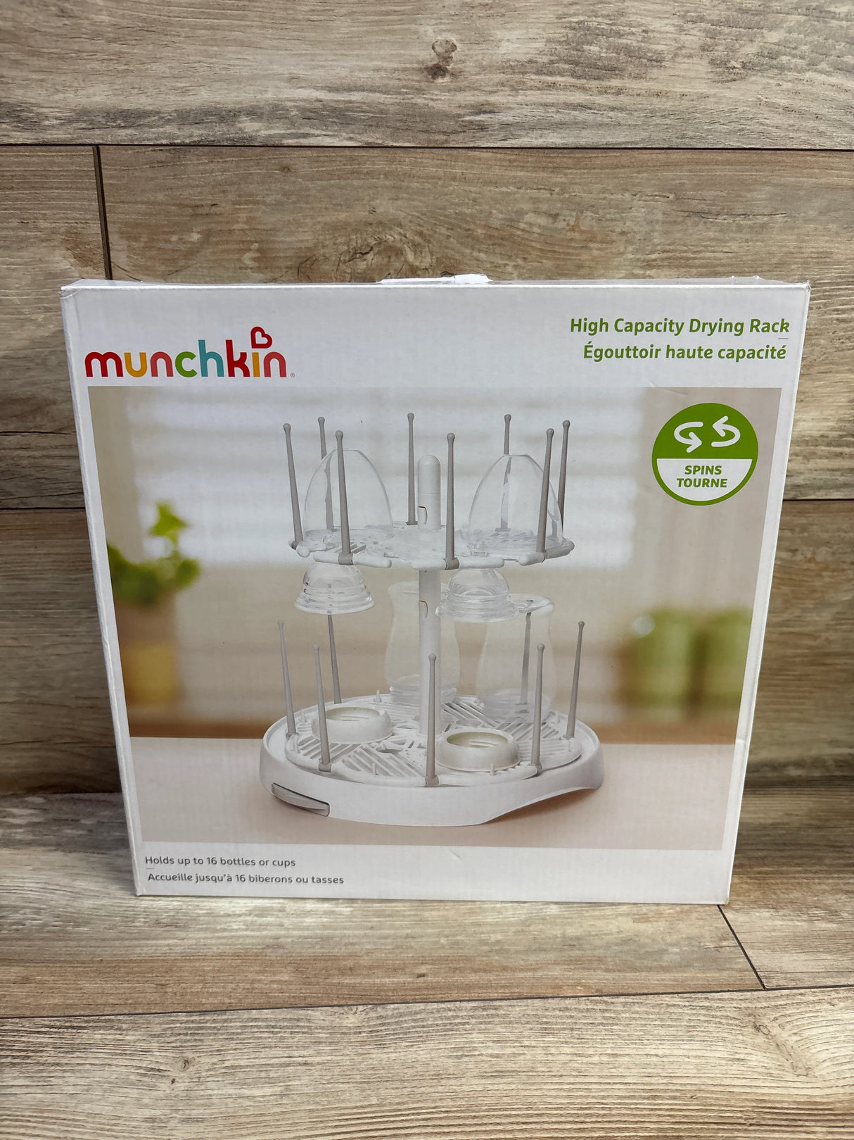 Front view of Munchkin high-capacity bottle drying rack box showing two-tier spinning white rack that holds up to 16 bottles on wooden background