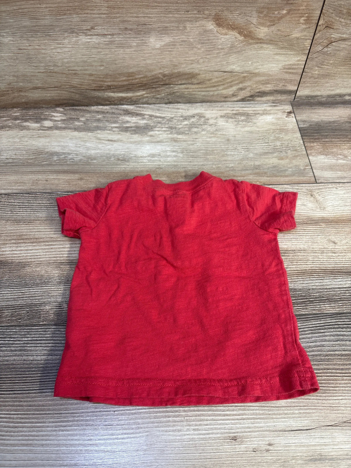 Back view of a red Just One You Henley shirt for infants size 12m on a wood background.