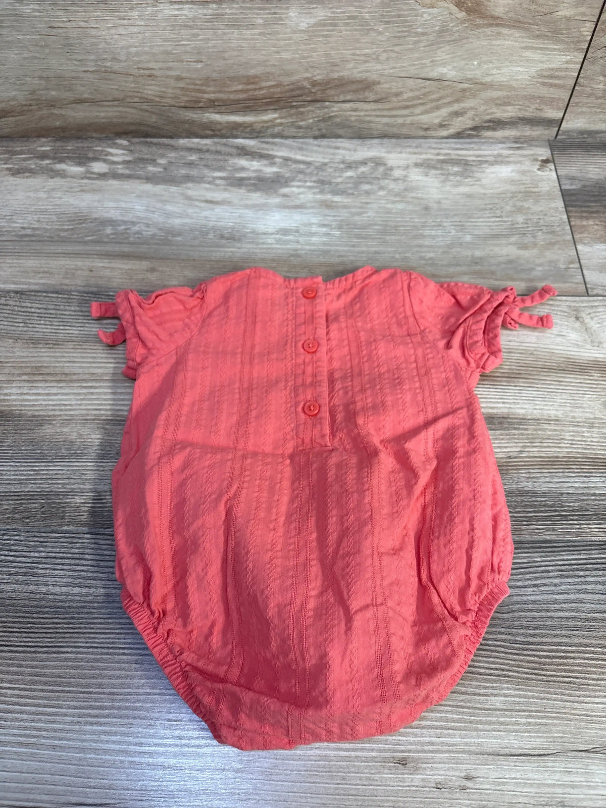 Top view of OshKosh hot pink bubble romper, size 3 months, with short sleeves, buttons, and textured cotton on wood surface