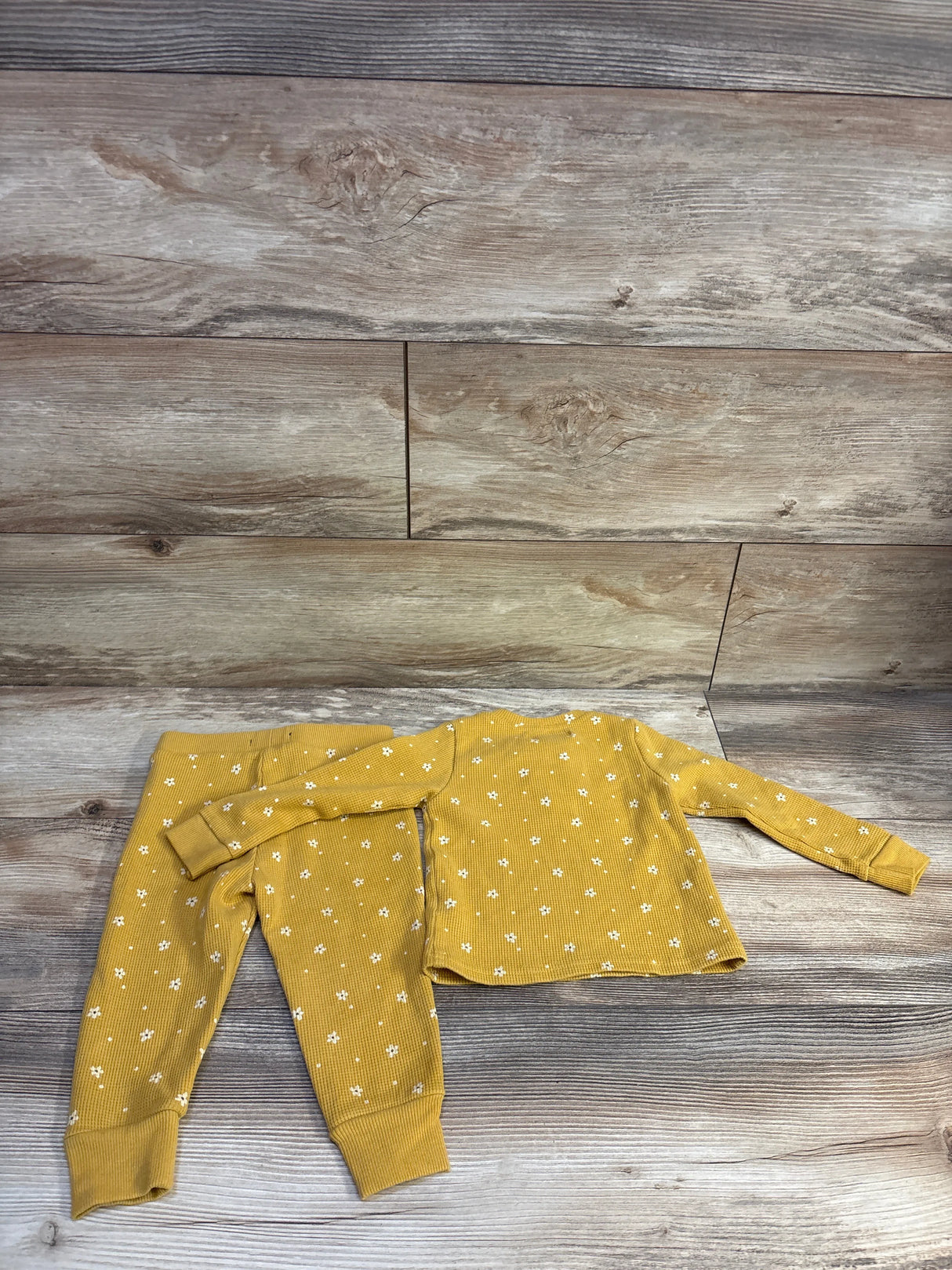 Flat lay of yellow waffle-knit henley top and pants with white floral print and ribbed cuffs on light wood background