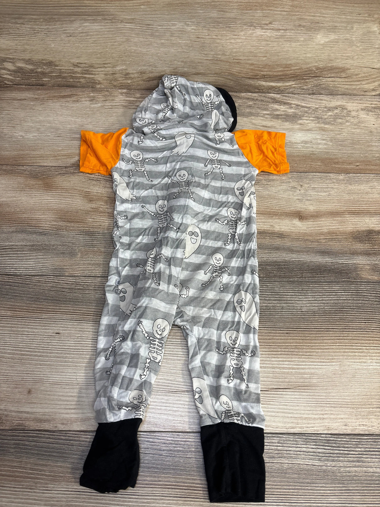 Gray striped baby Halloween romper with skeletons, orange sleeves, black cuffs, laid on wood floor
