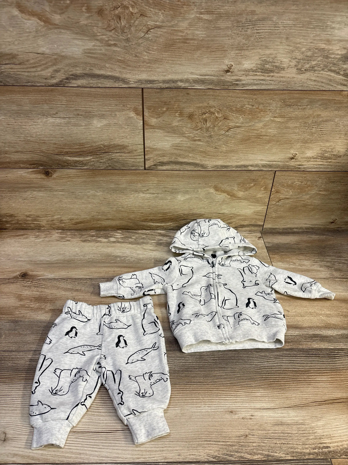 Top down view of Carter’s grey 2 piece zip up jacket and pants set showcasing animal prints and ribbed cuffs on a wood floor
