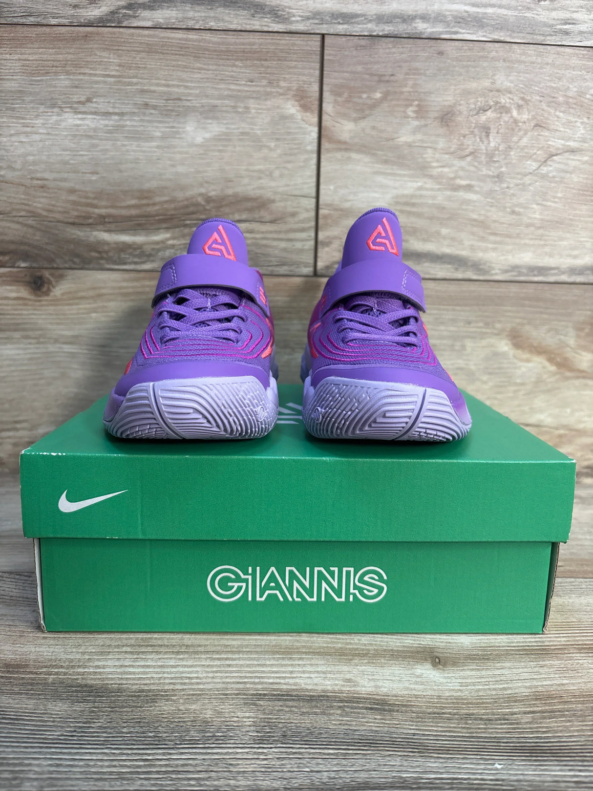 Purple and pink youth Nike Giannis basketball shoes on green shoebox, wooden floor background