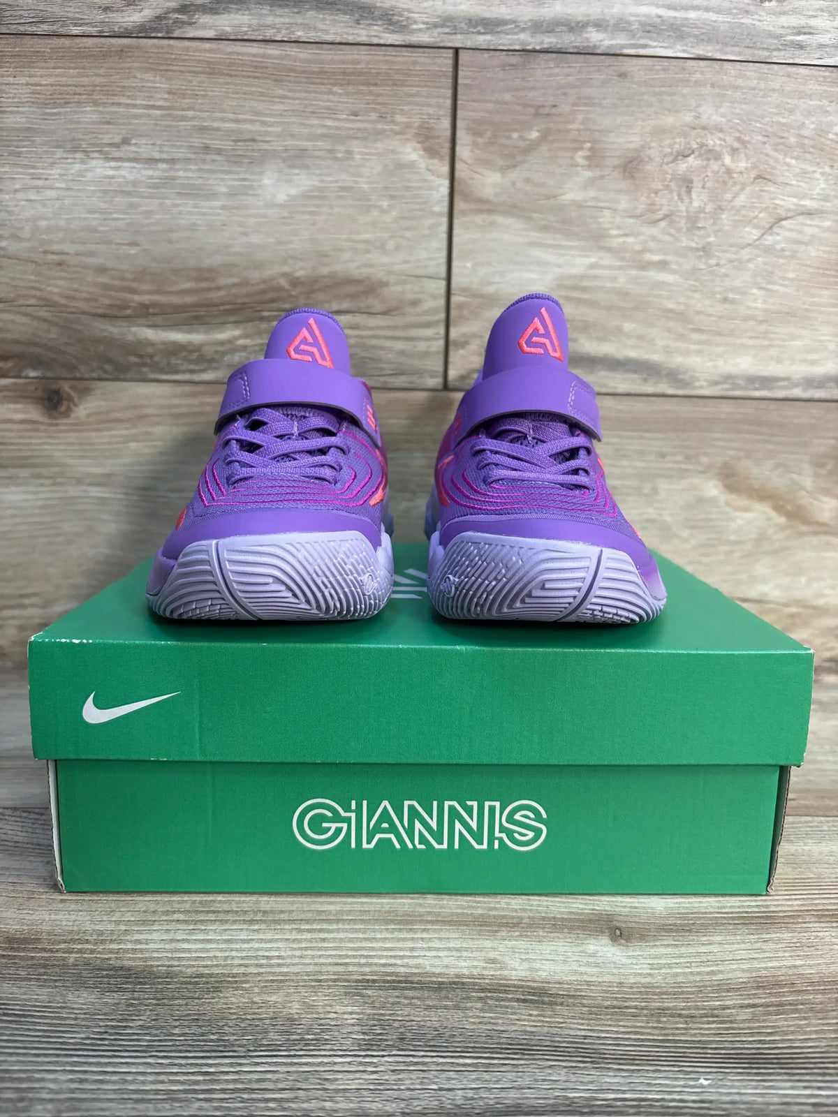 Purple and pink youth Nike Giannis basketball shoes on green shoebox, wooden floor background