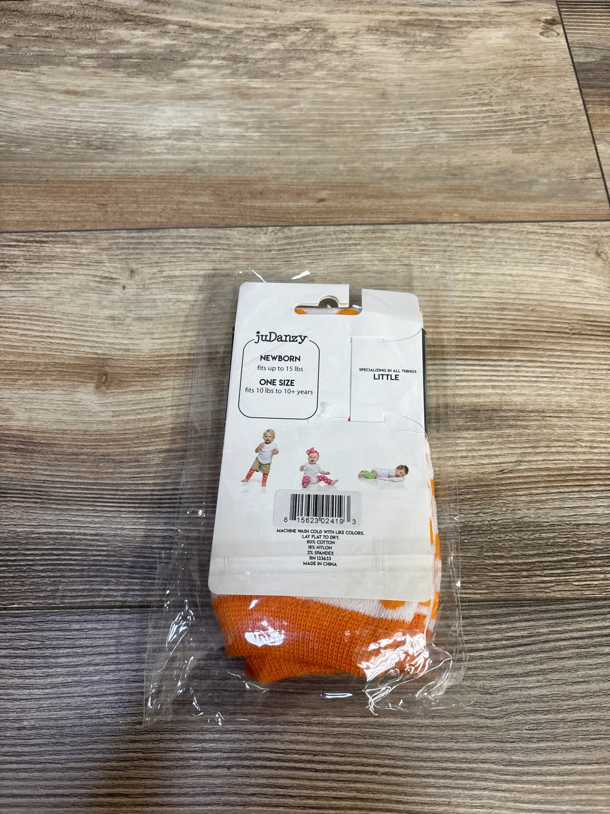 Front view of JuDanzy Halloween polka dot leg warmers, orange and white, packaged on a wood-grain surface