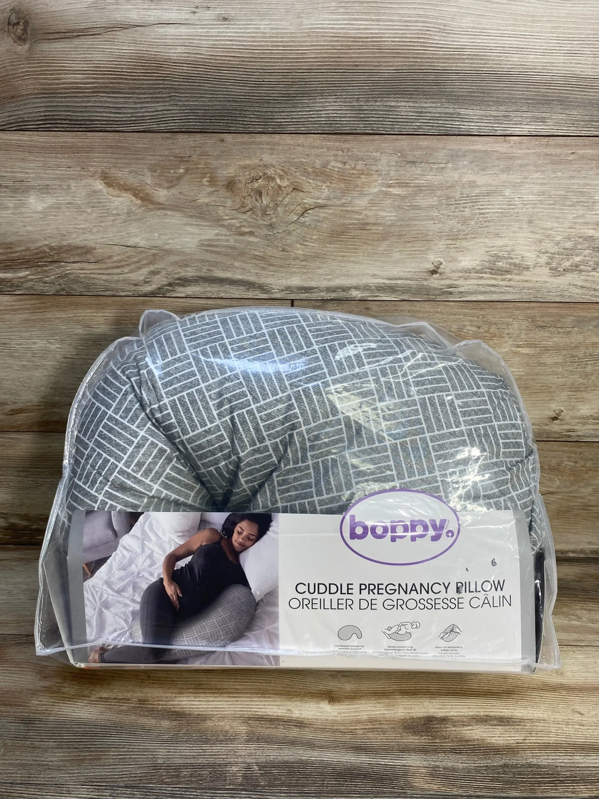 Front view of Boppy Cuddle pregnancy pillow in gray basket weave slipcover inside clear packaging on wood floor