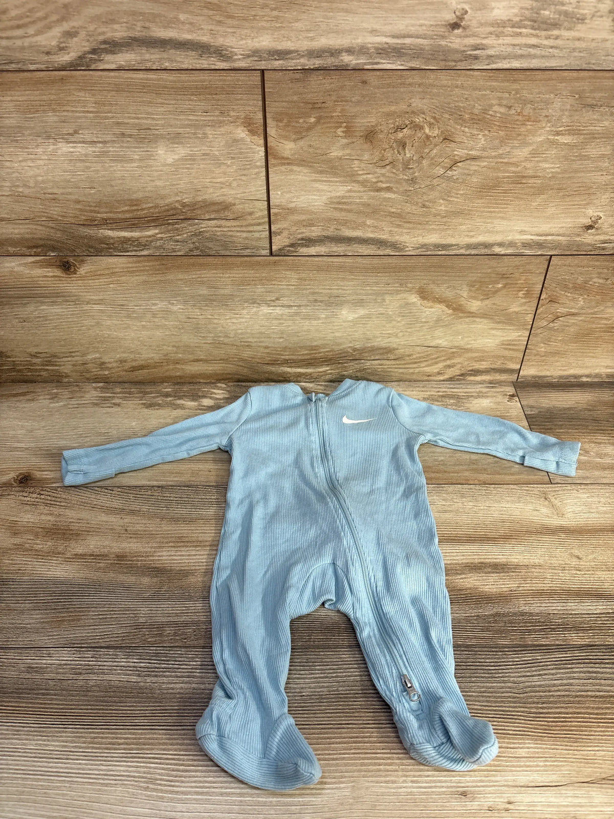 Front view of Nike blue ribbed sleeper showcasing footed legs and front zipper with wooden floor background