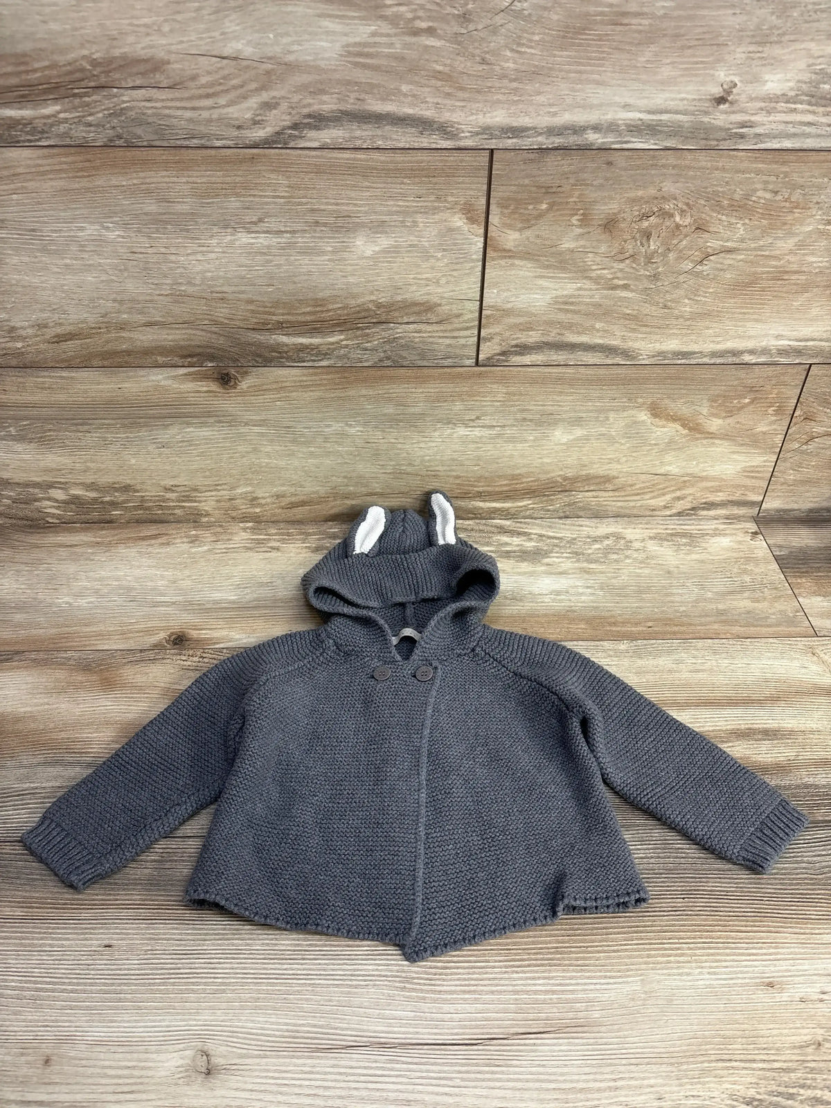 Gray knit baby sweater with hood and ear details, laid flat on wood background