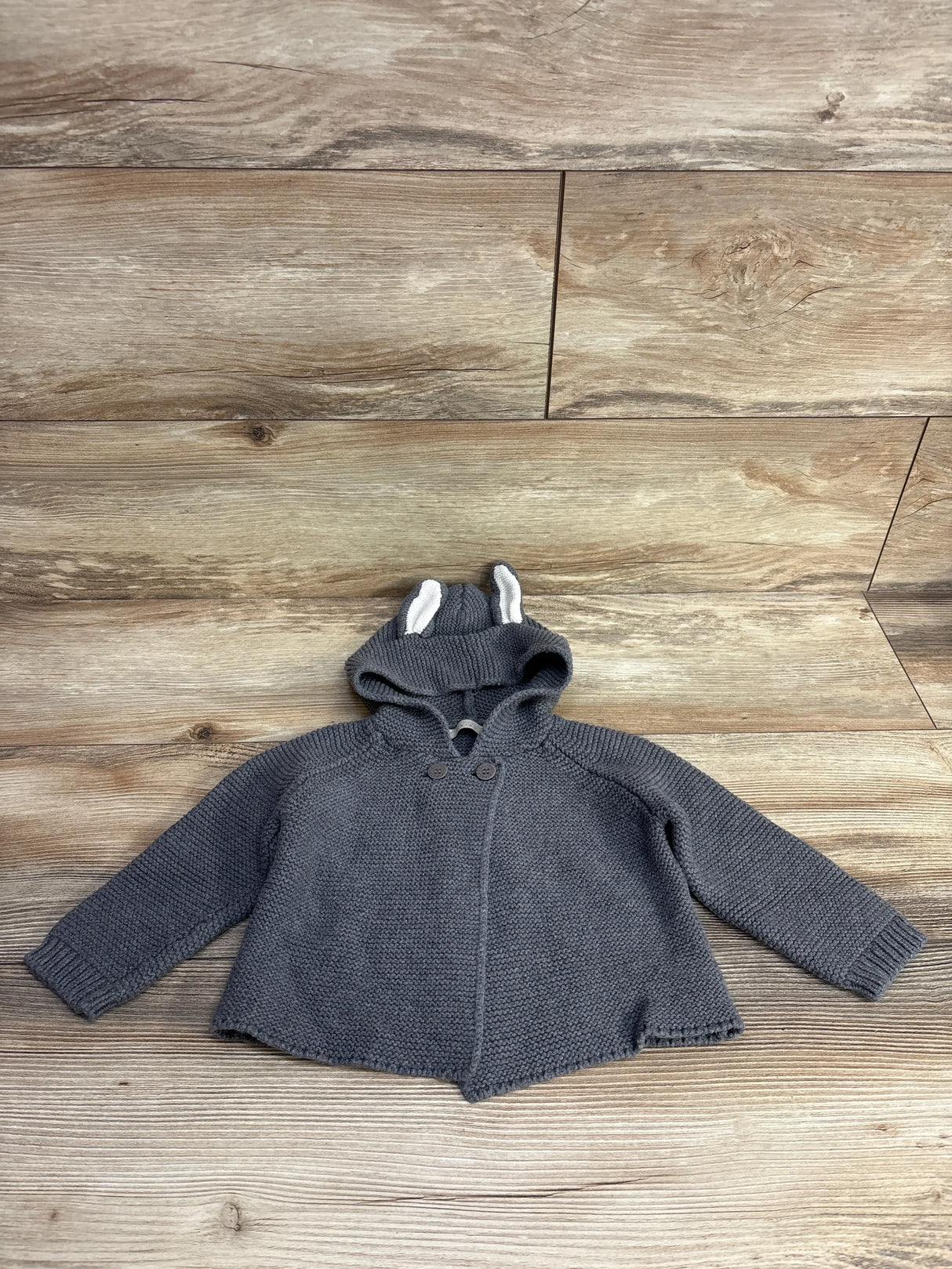 Gray knit baby sweater with hood and ear details, laid flat on wood background
