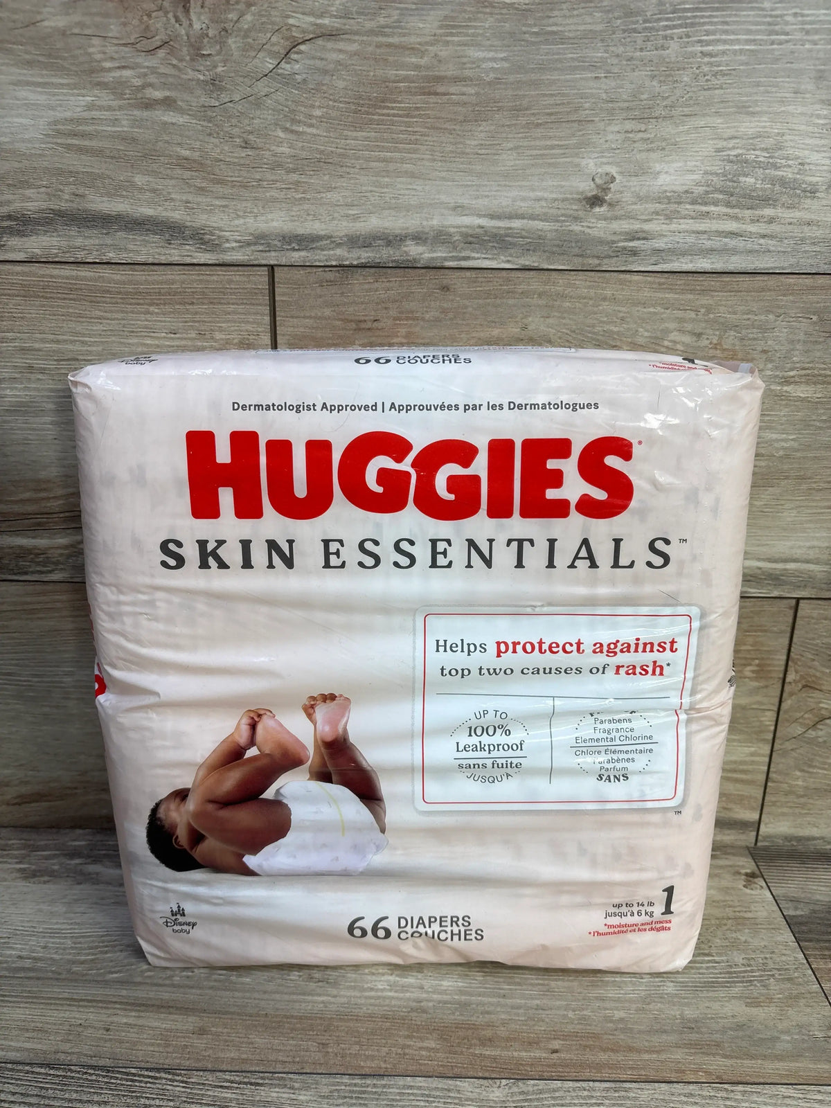 Front view of new Huggies Skin Essentials Diapers Size 1 66 count package showing rash protection on a wood look surface