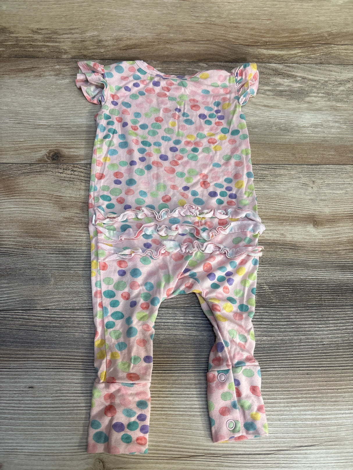 Pink baby romper with colorful polka dots, ruffle sleeves and ruffle waist, laid on wood background