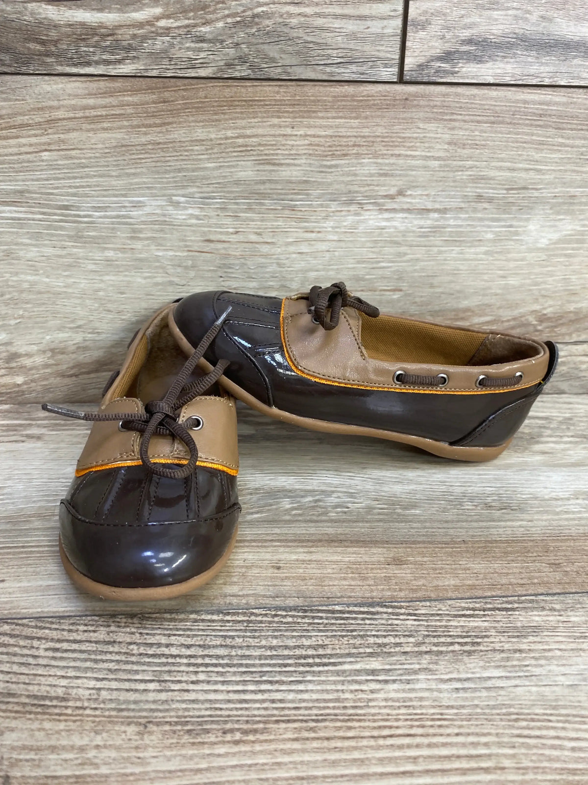 Front view of Balleto toddler boat shoes showcasing glossy dark-brown toe, tan collar and orange trim on wood background