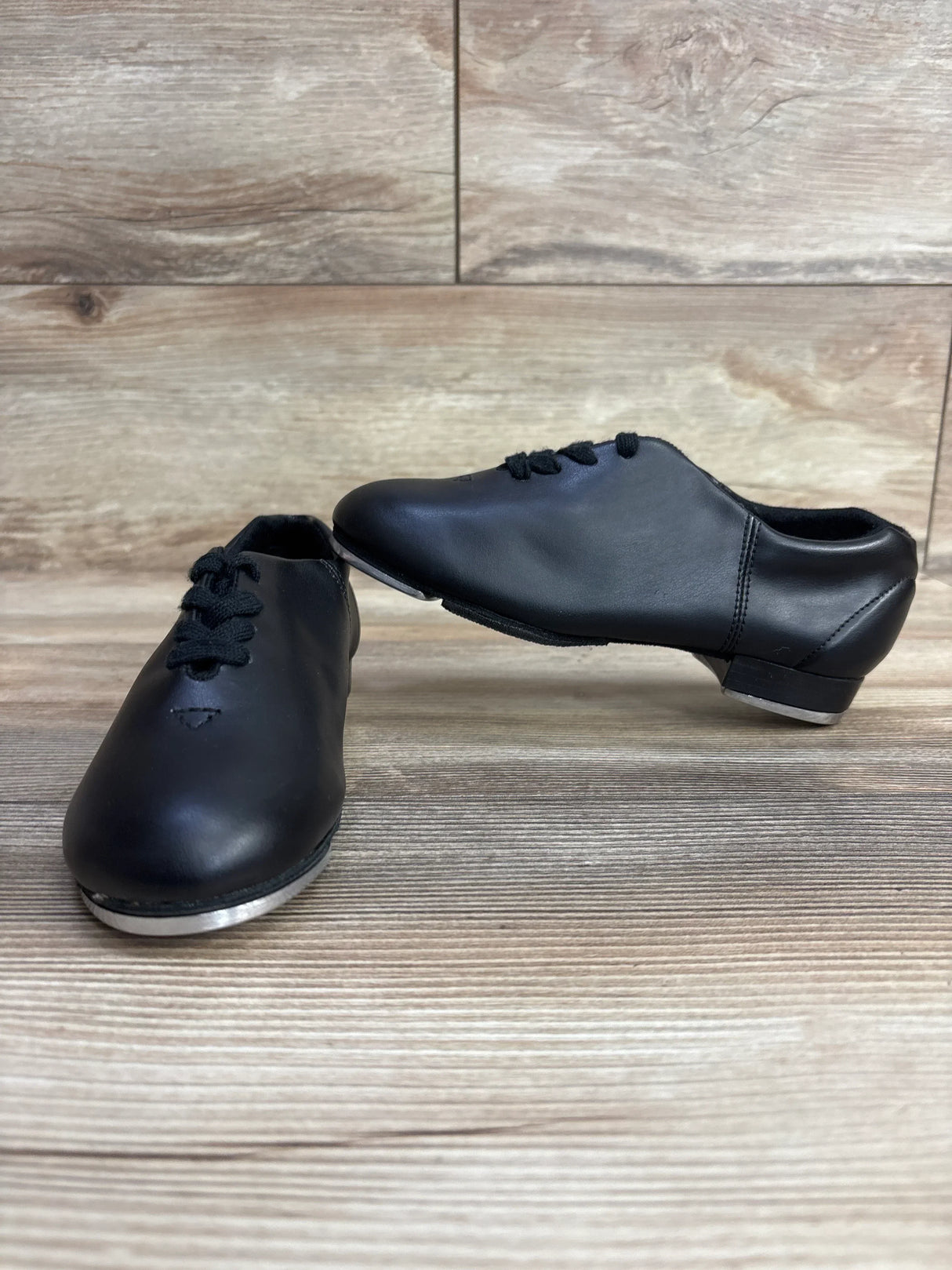 Pair of black leather tap dance shoes with laces on wood background, kids' dance footwear