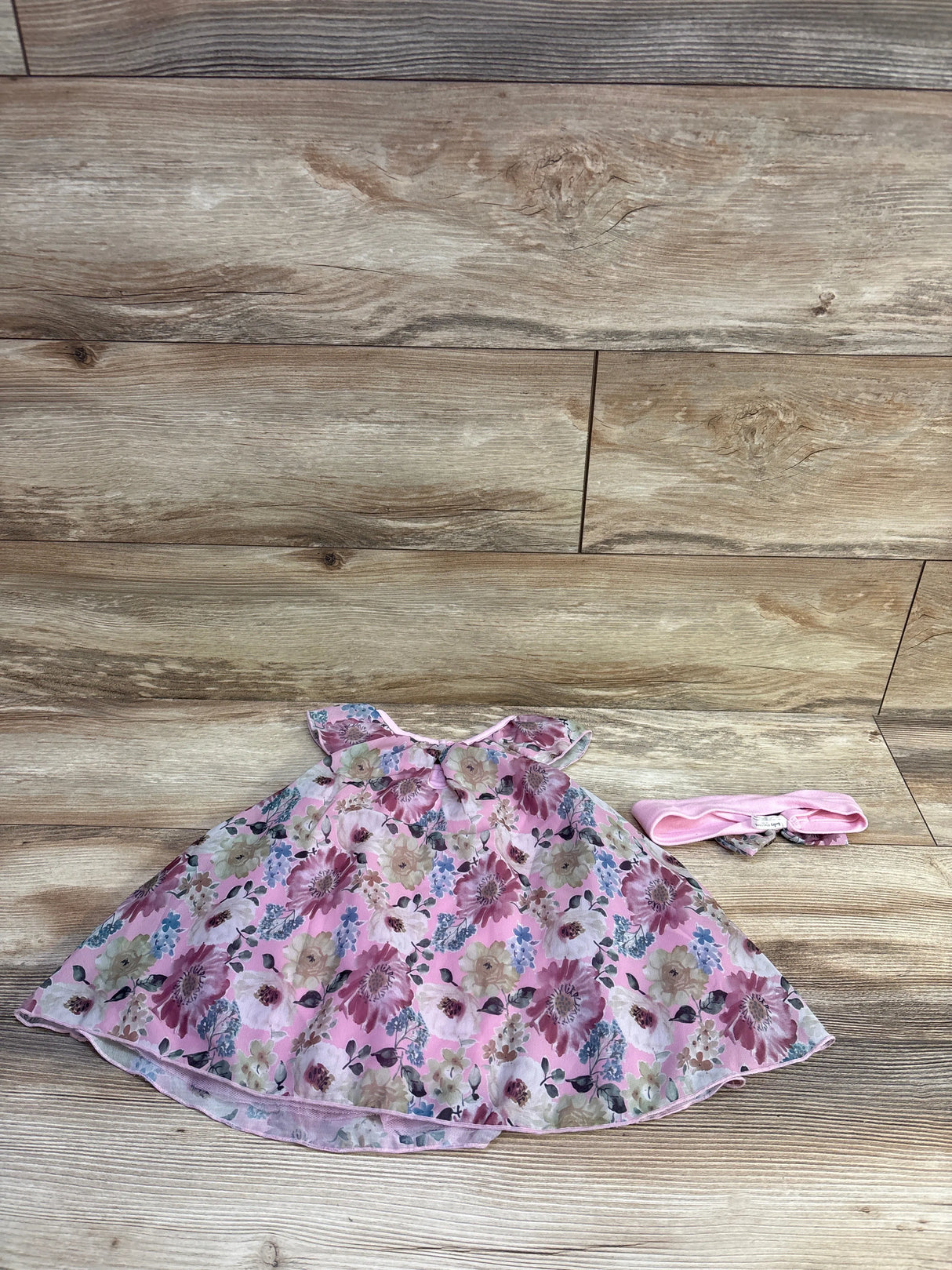 Flat lay of pink Baby Starters 2-piece bodysuit dress and matching headband showcasing floral print on wood background