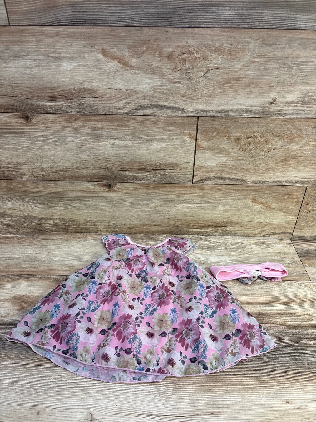 Flat lay of pink Baby Starters 2-piece bodysuit dress and matching headband showcasing floral print on wood background