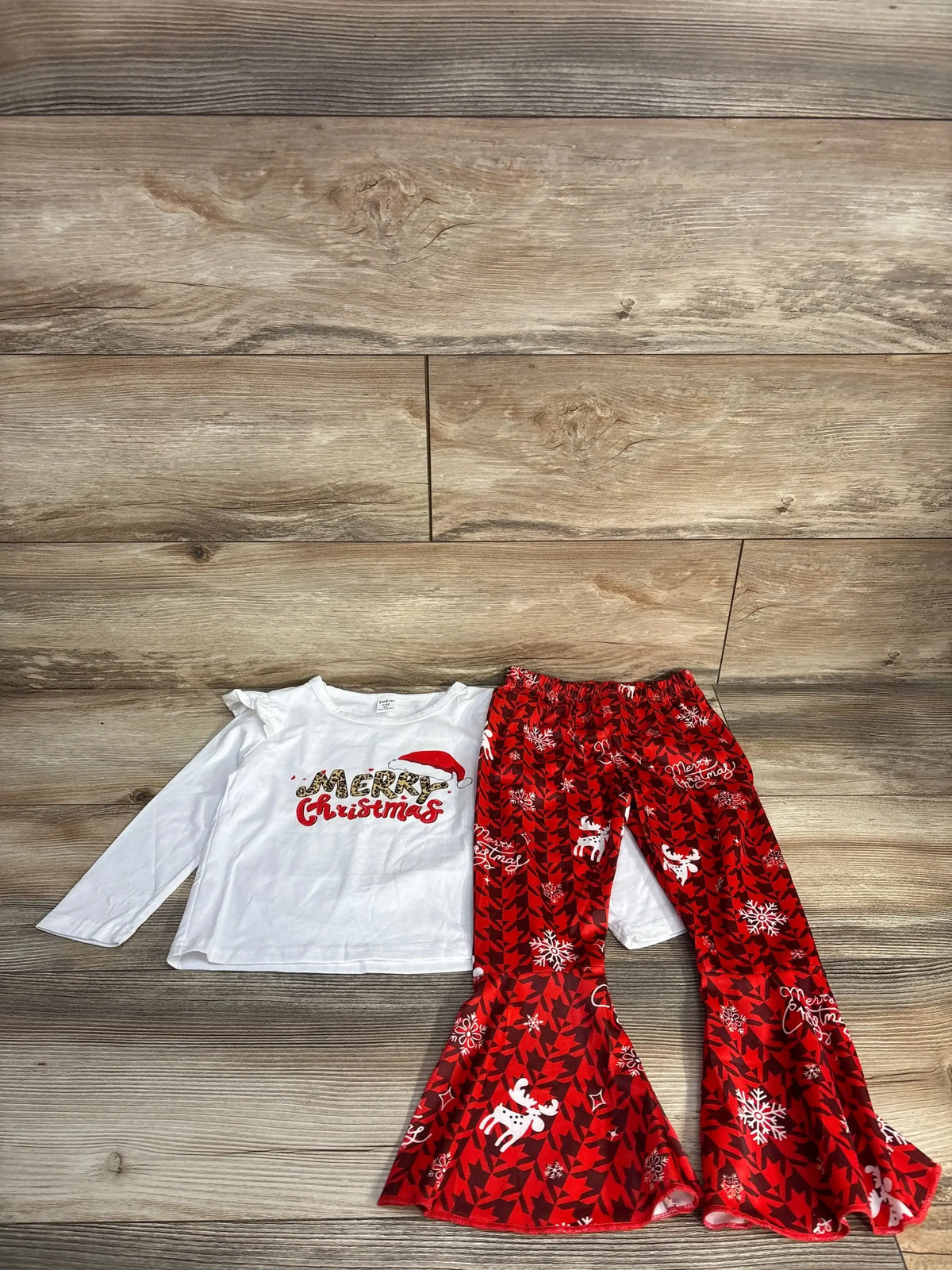 Kids Christmas outfit with white long sleeve top and red bell-bottom pants on wood floor