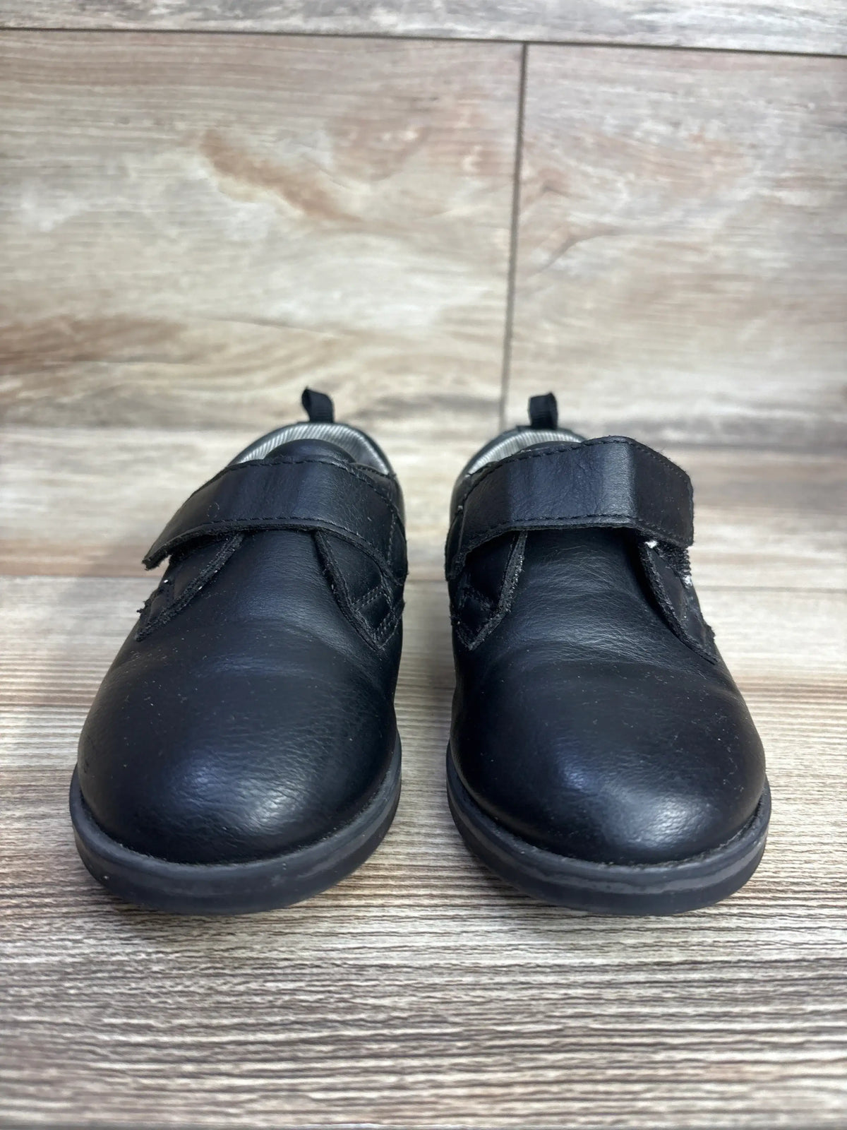 Front view of Wonder Nation Oxford dress shoes in black showcasing hook and loop strap closure and rounded toe on wood plank floor