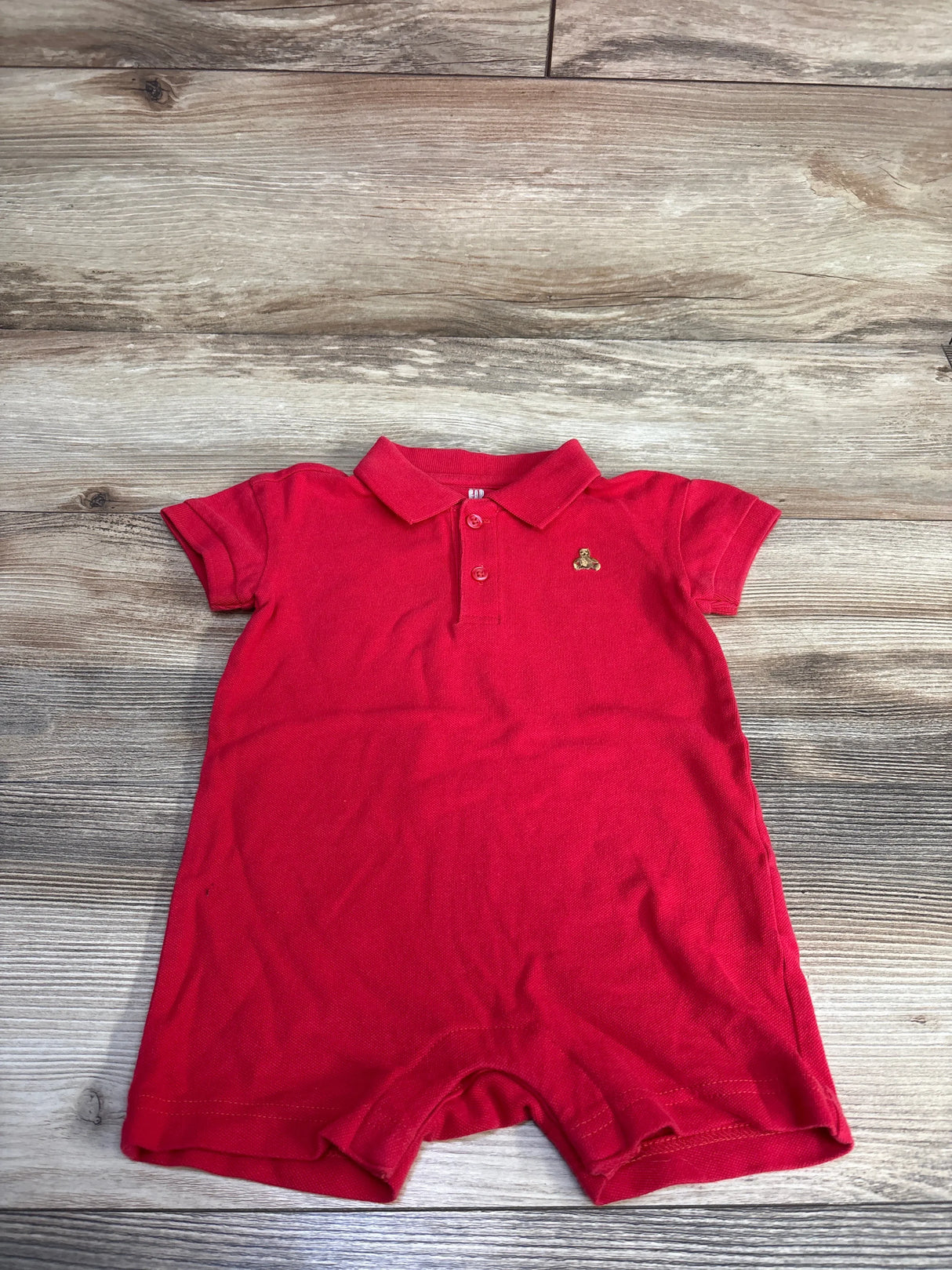 Front view of Baby Gap red henley romper with collar, button placket, sleeves, embroidered chest logo on wood floor