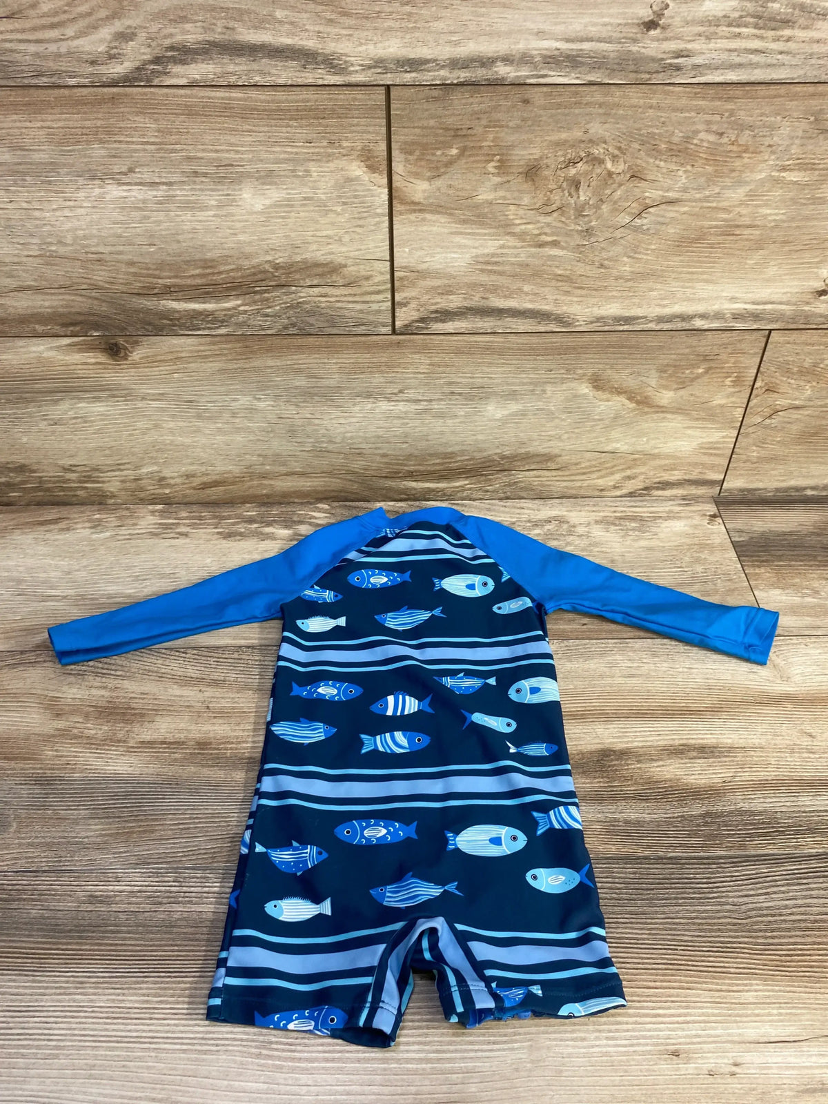 Flat-lay of Bonverano one-piece rashguard swimsuit 3-6 months with blue fish print and blue long sleeves on wood floor