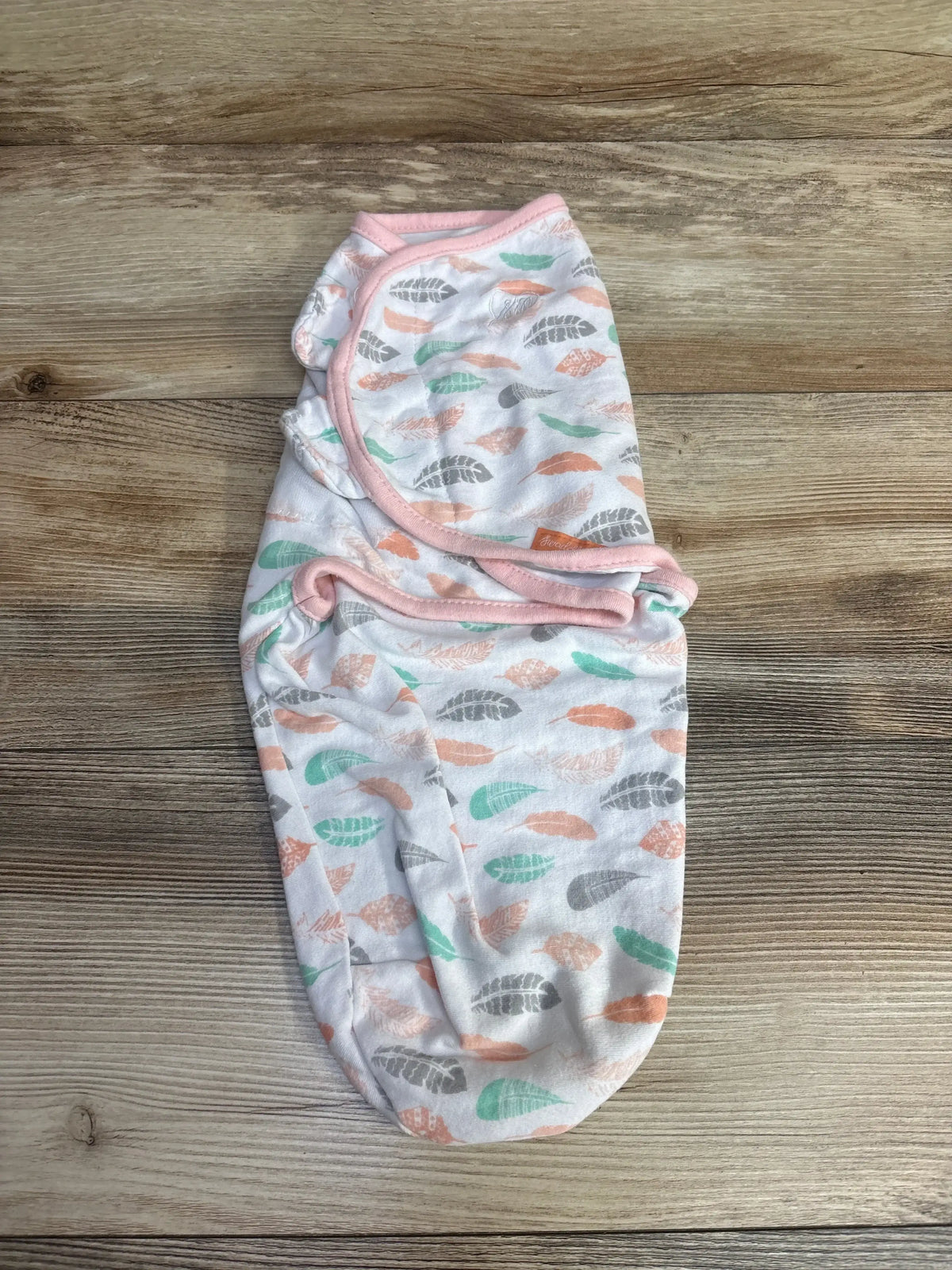 Folded baby swaddle blanket with pastel feather print on wooden surface