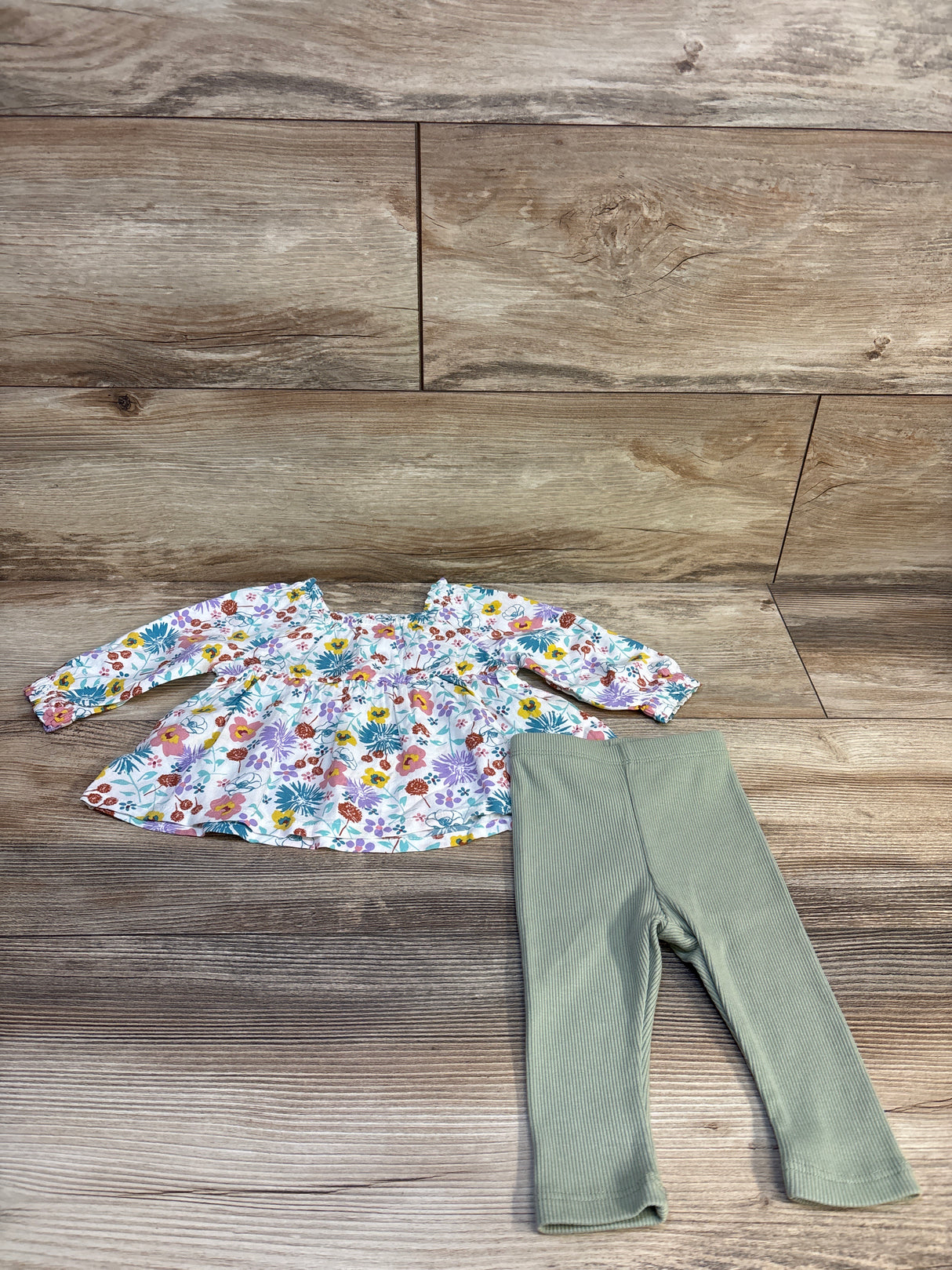 Flat lay of Okie Dokie 2-piece floral long-sleeve baby top with ruffled sleeves and sage ribbed leggings on wood floor