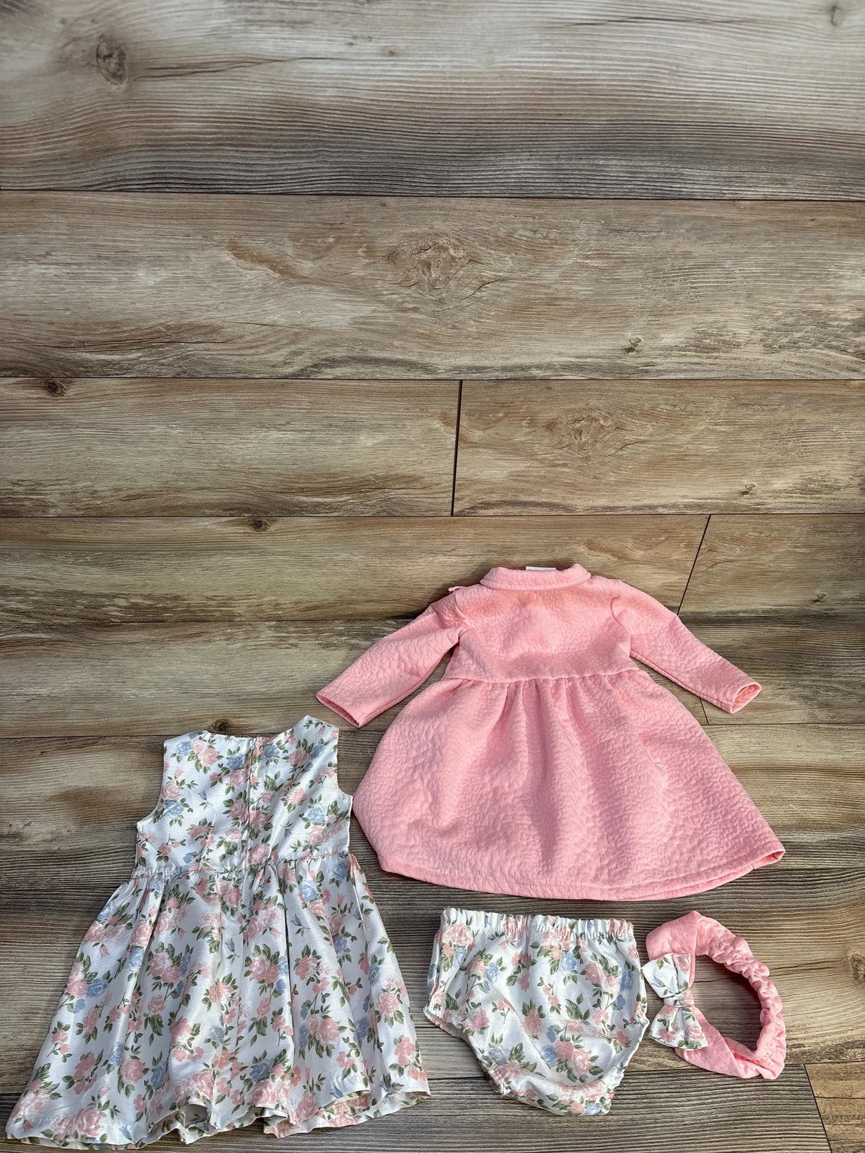 Pink long-sleeve baby dress with floral bloomers, headband, and matching sleeveless dress on wood floor