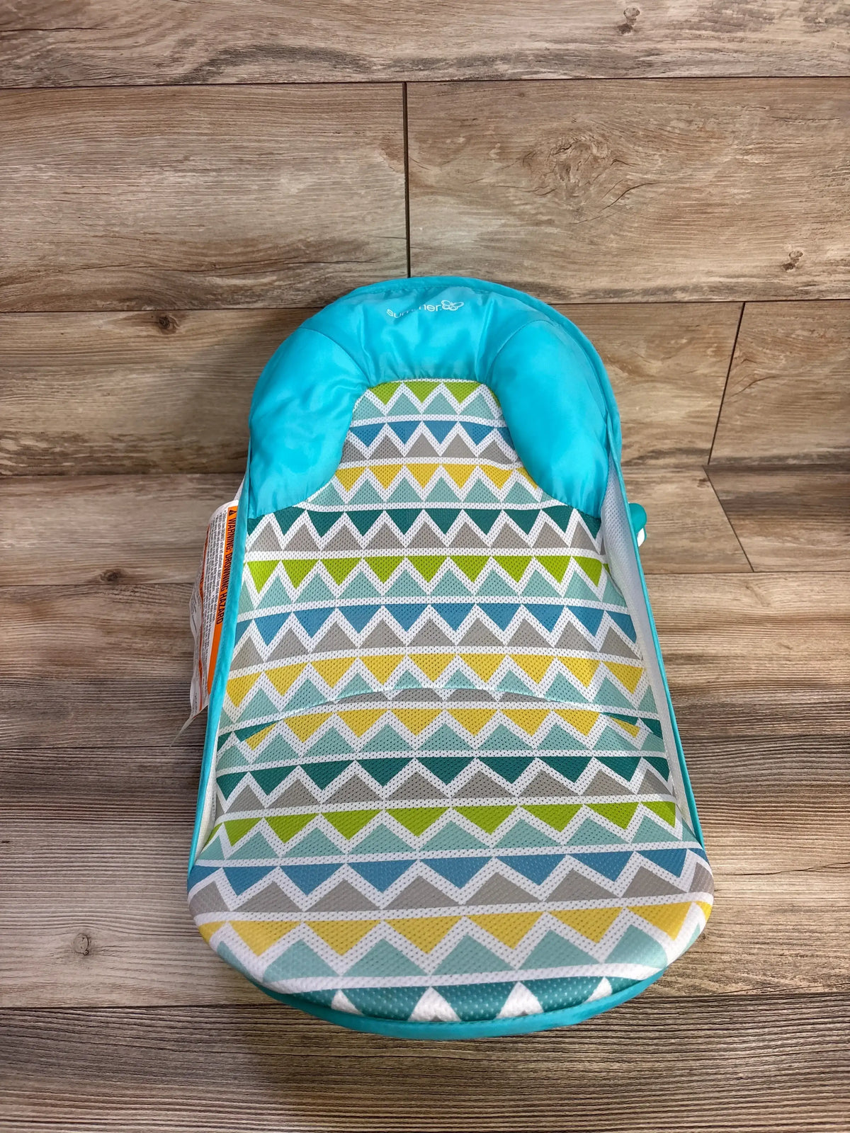 Top-down view of Summer Deluxe Baby Bather in teal and green showcasing padded headrest and geometric chevron mesh fabric with wood floor background