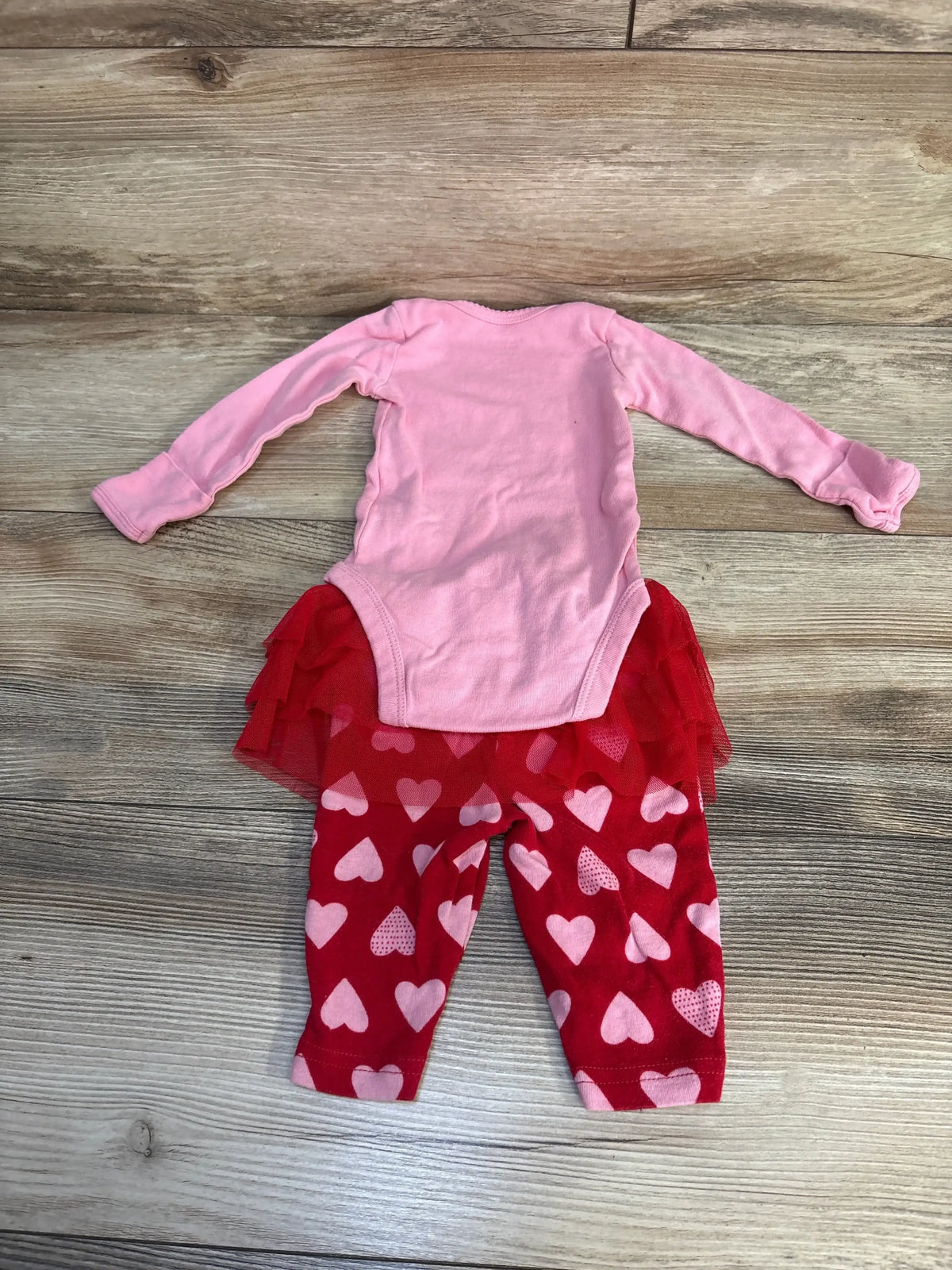 Pink long sleeve baby bodysuit with red tutu and heart print leggings on wood floor