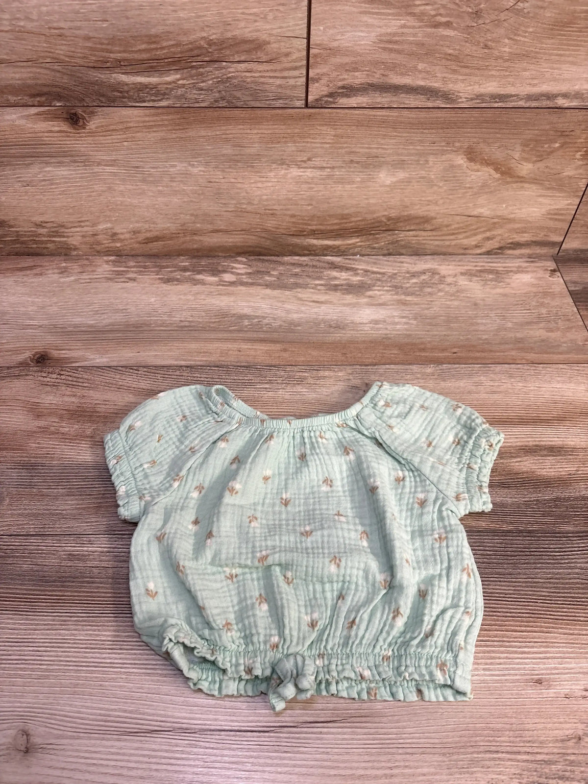 Front flat lay of green gauze toddler shirt size 2T showing short elastic sleeves, drawstring hem and small floral print on wood
