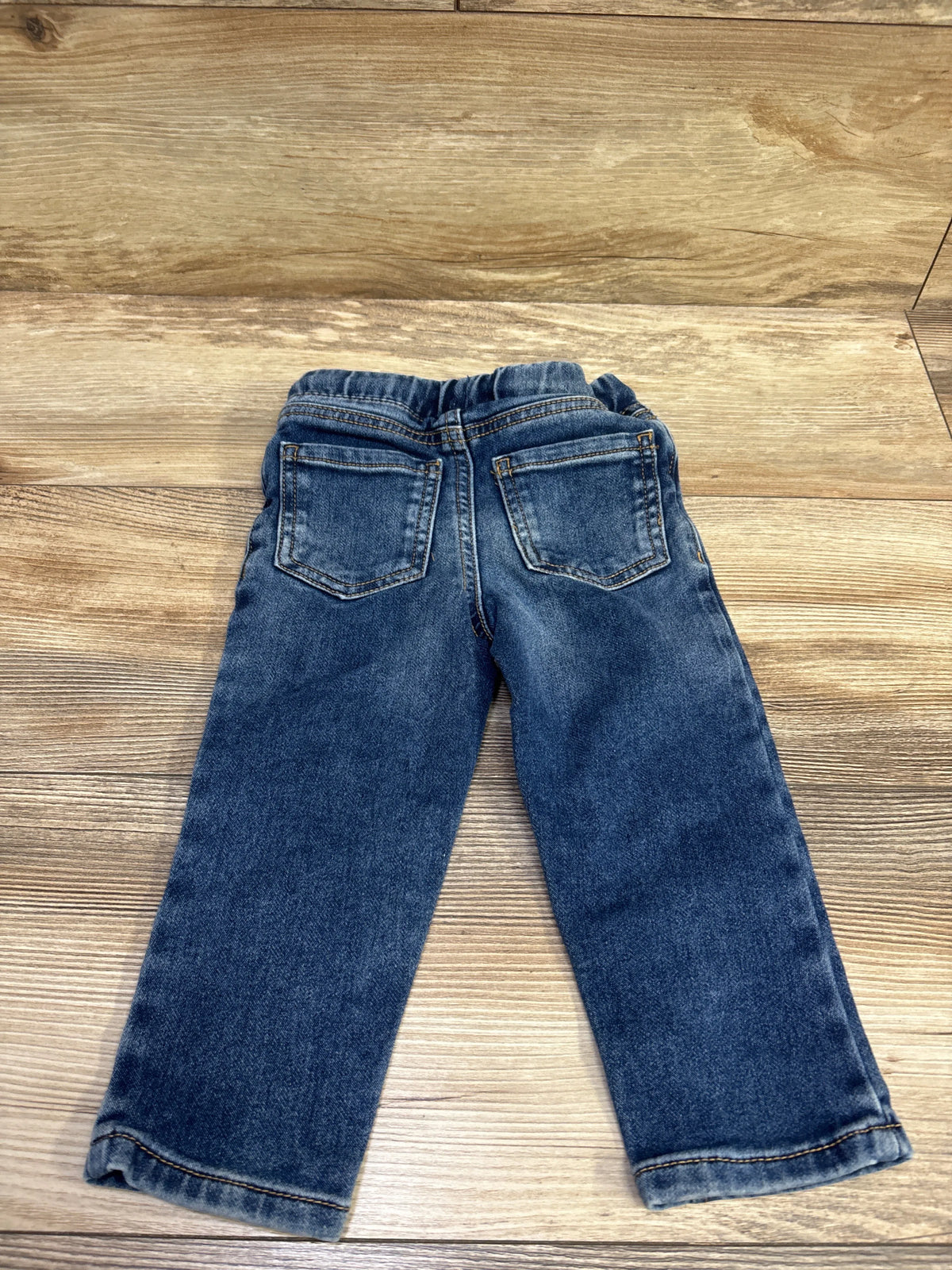 Back view of Okie Dokie drawstring jeans in blue showcasing two back pockets and cuffed hems with wood background