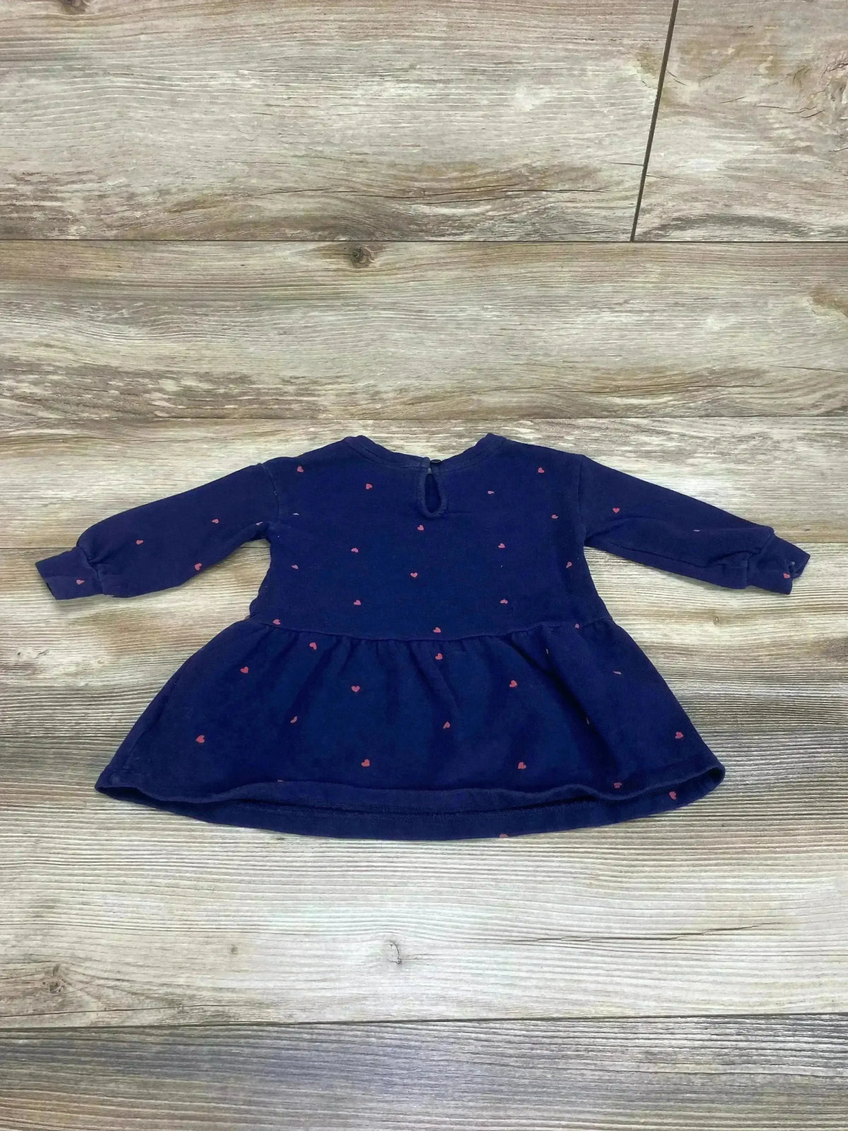 Flat lay of Baby Gap navy sweatshirt dress showing long sleeves, gathered skirt, and small pink heart print on light wood background