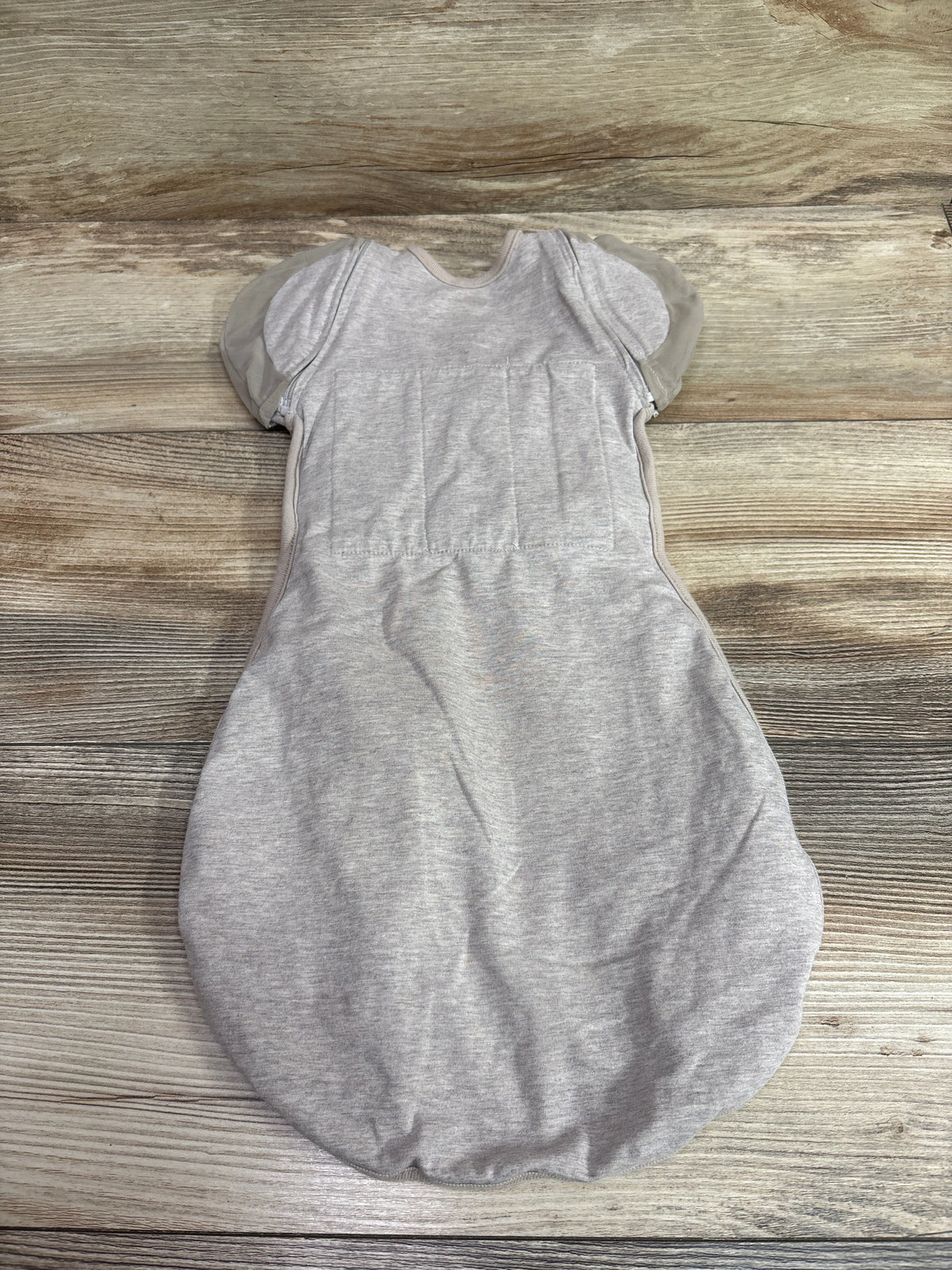 Front view of Nested Bean Zen One Classic Convertible Swaddle in beige showcasing short sleeves on a wood background