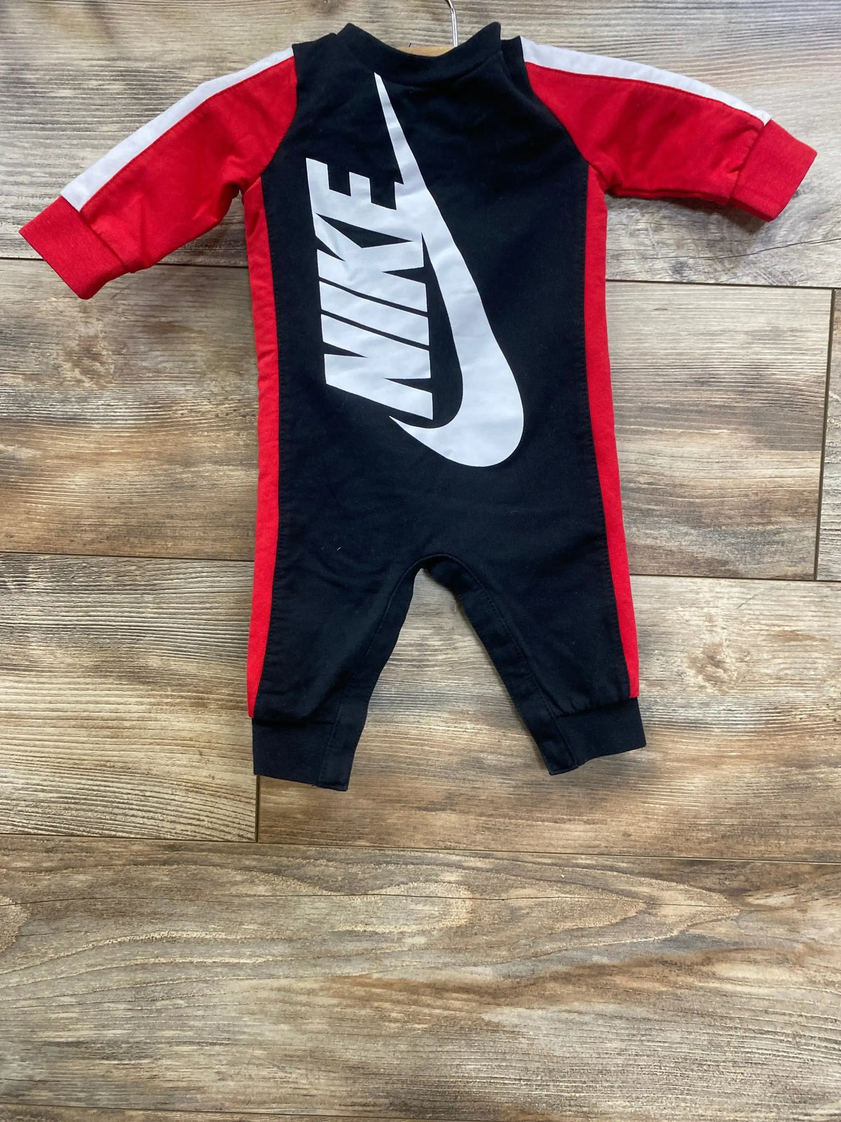 Nike baby romper, black with red sleeves, bold logo, laid flat on wood floor