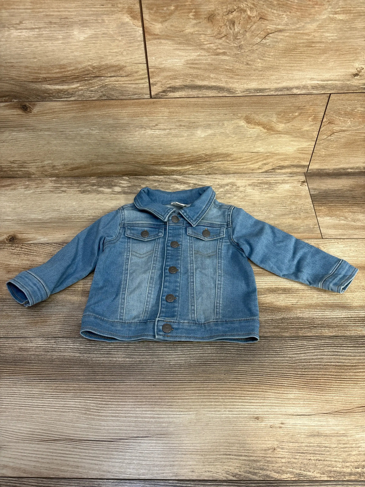 Blue denim toddler jacket with long sleeves and buttons on wooden floor background