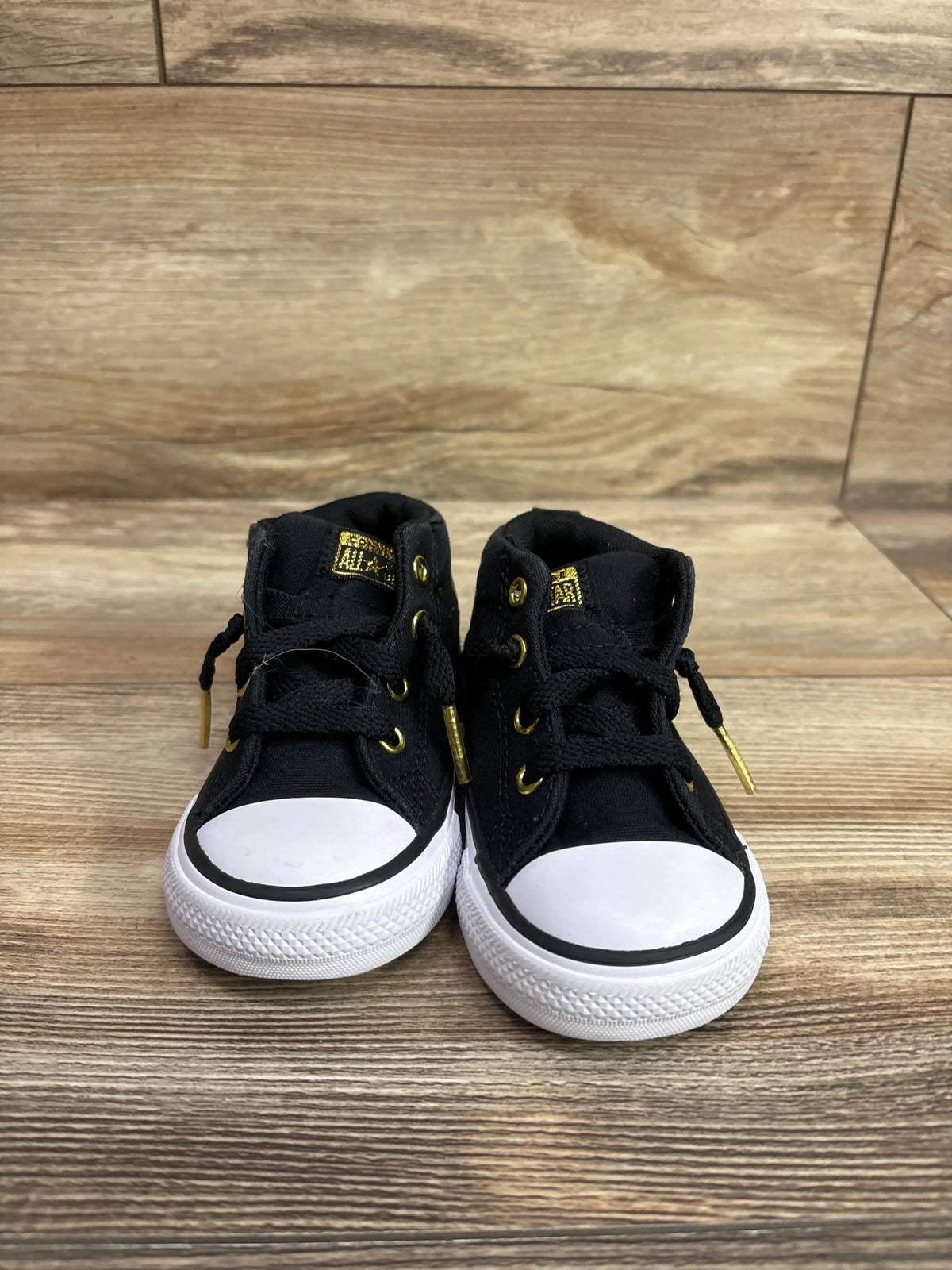 Front view of black Converse Chuck Taylor All Star Street mid sneakers showing white toe caps and soles on wood flooring