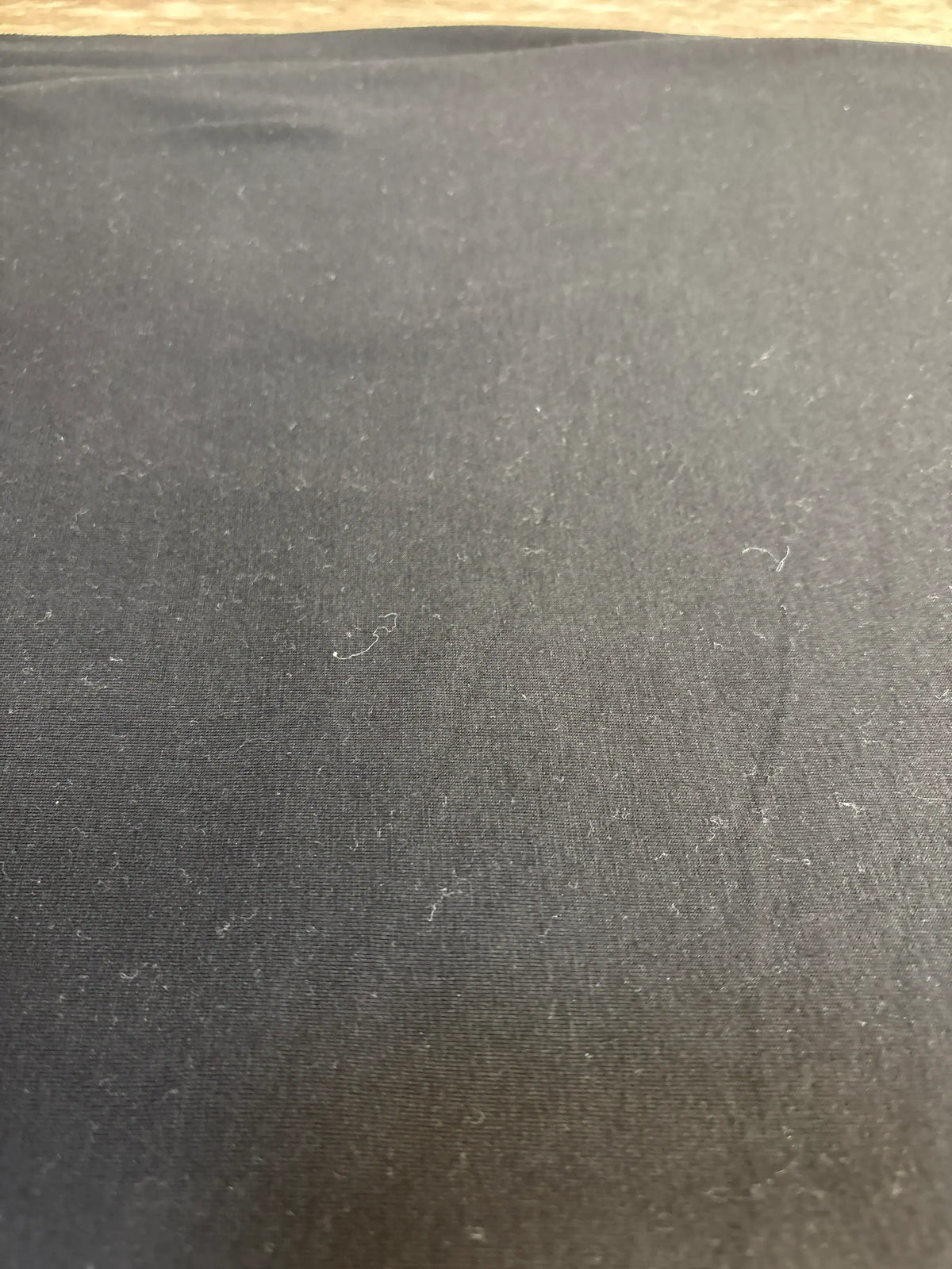 Close-up of Copper Pearl Knit Swaddle Blanket in black showing knit texture and scattered lint with wooden floor edge