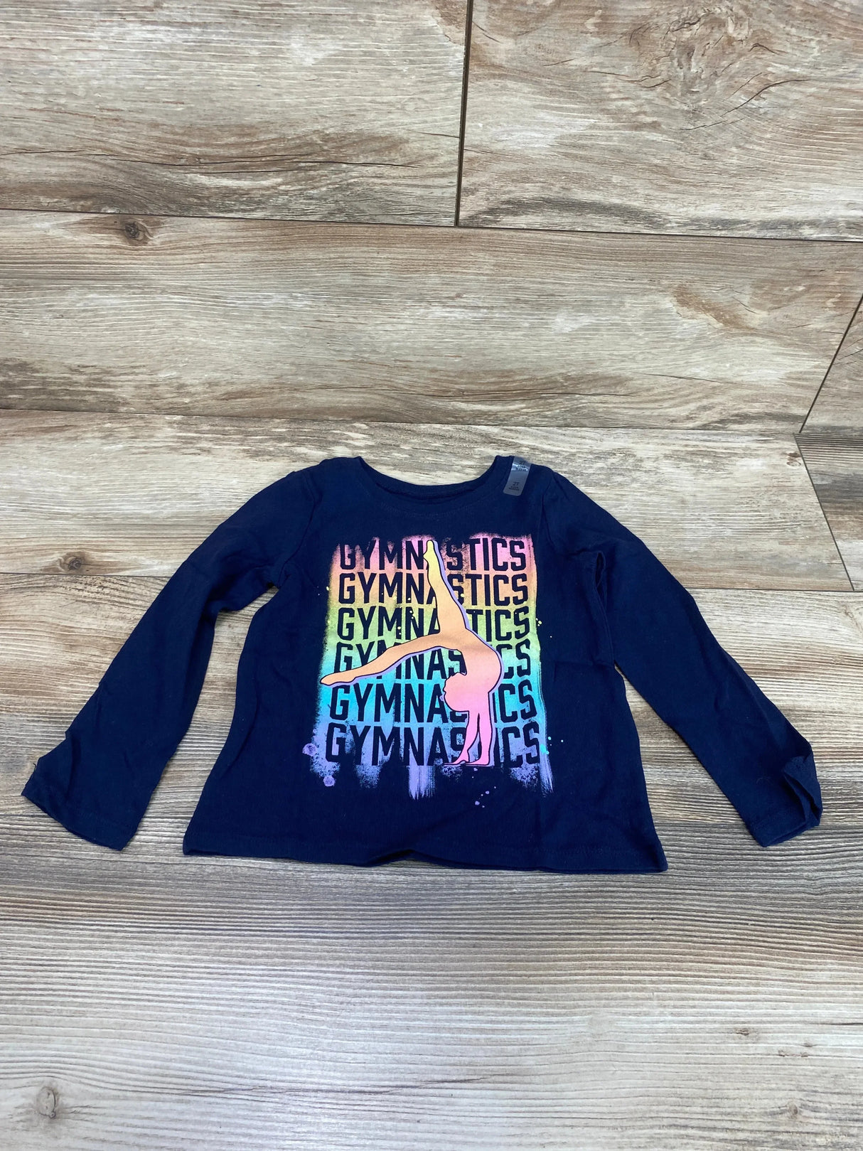 Front view of Children's Place navy long-sleeve toddler (2T) gymnastics shirt showing rainbow GYMNASTICS print and pink gymnast on wood floor